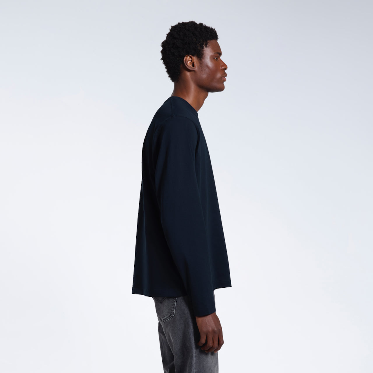 A man facing side on with his arms by his sides, modelling a plain navy long sleeve organic cotton t shirt.