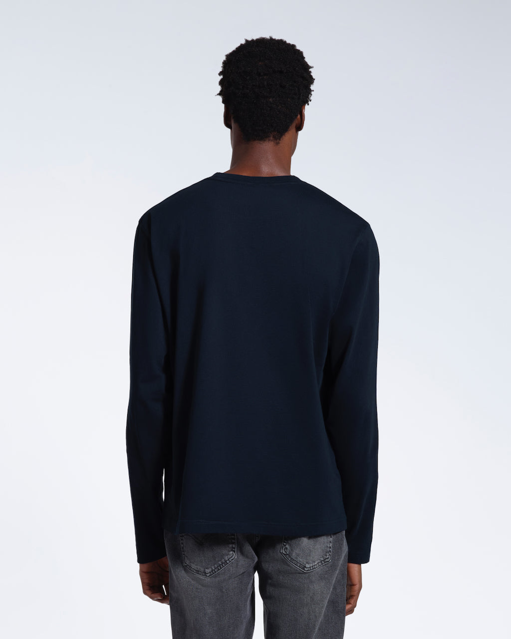 A man facing away from the camera with his arms by his sides, modelling a plain navy long sleeve organic cotton t shirt.