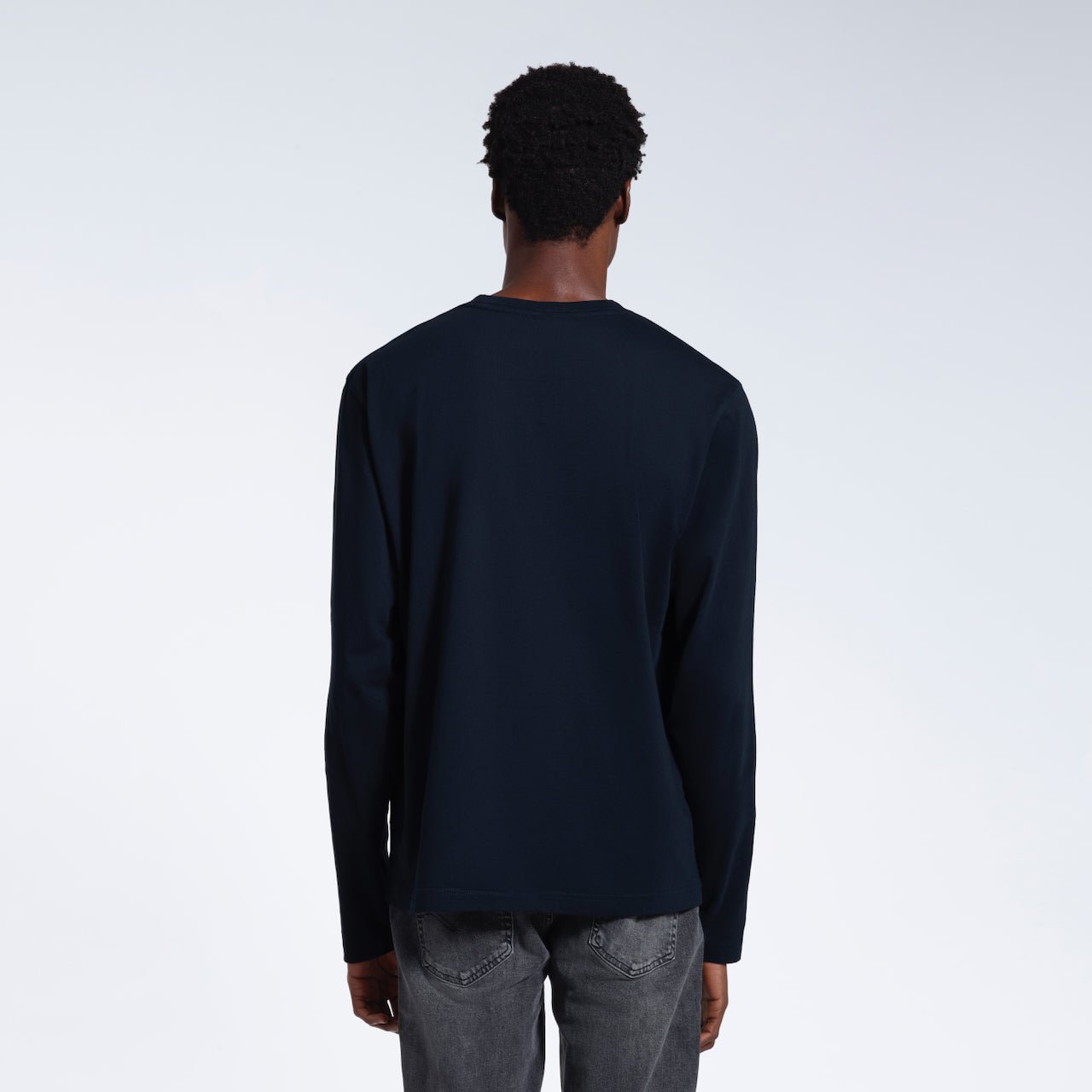 A man facing away from the camera with his arms by his sides, modelling a plain navy long sleeve organic cotton t shirt.