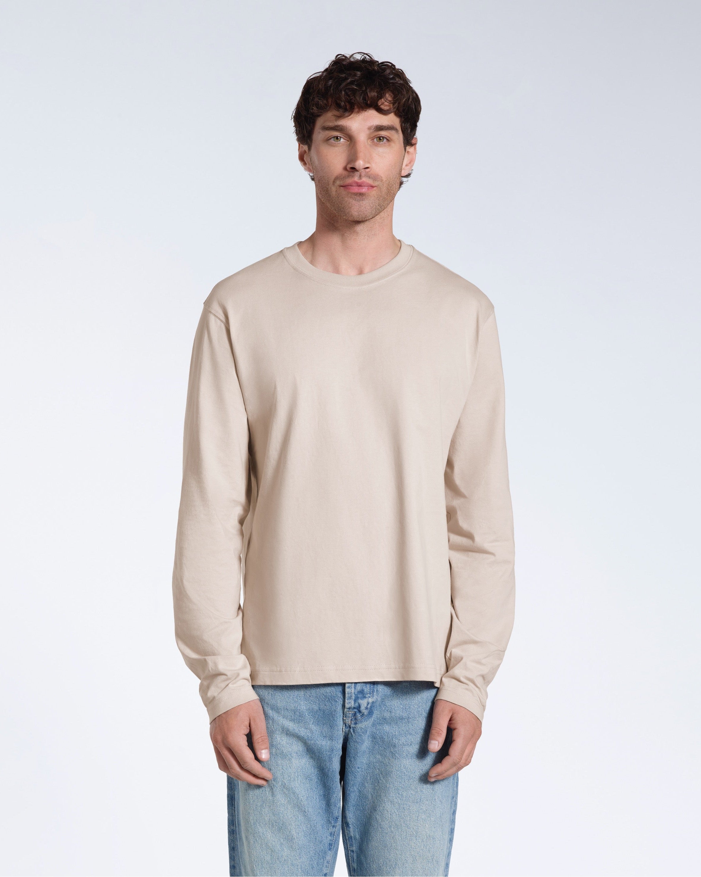 A man standing front on with his arms by his sides, modelling a plain stone long sleeve organic cotton t shirt.