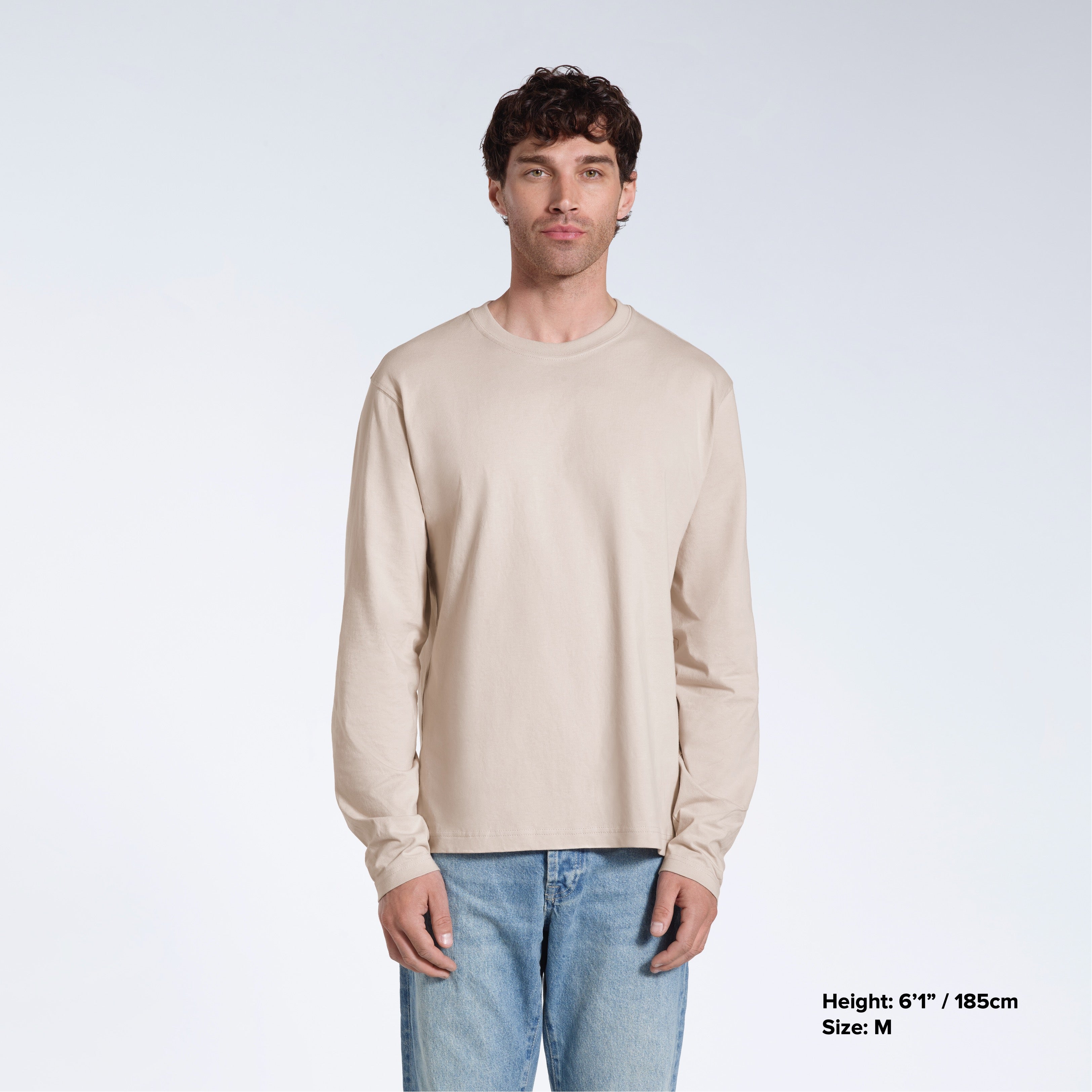 A man standing front on with his arms by his sides, modelling a plain stone long sleeve organic cotton t shirt.