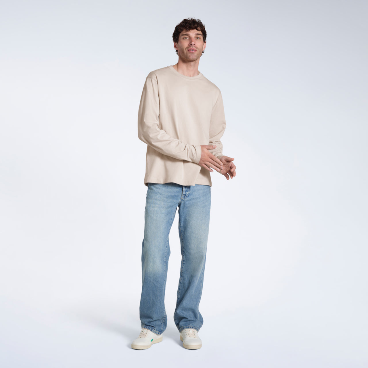 A full body photo of a man looking into the camera, modelling a plain stone long sleeve organic cotton t shirt.