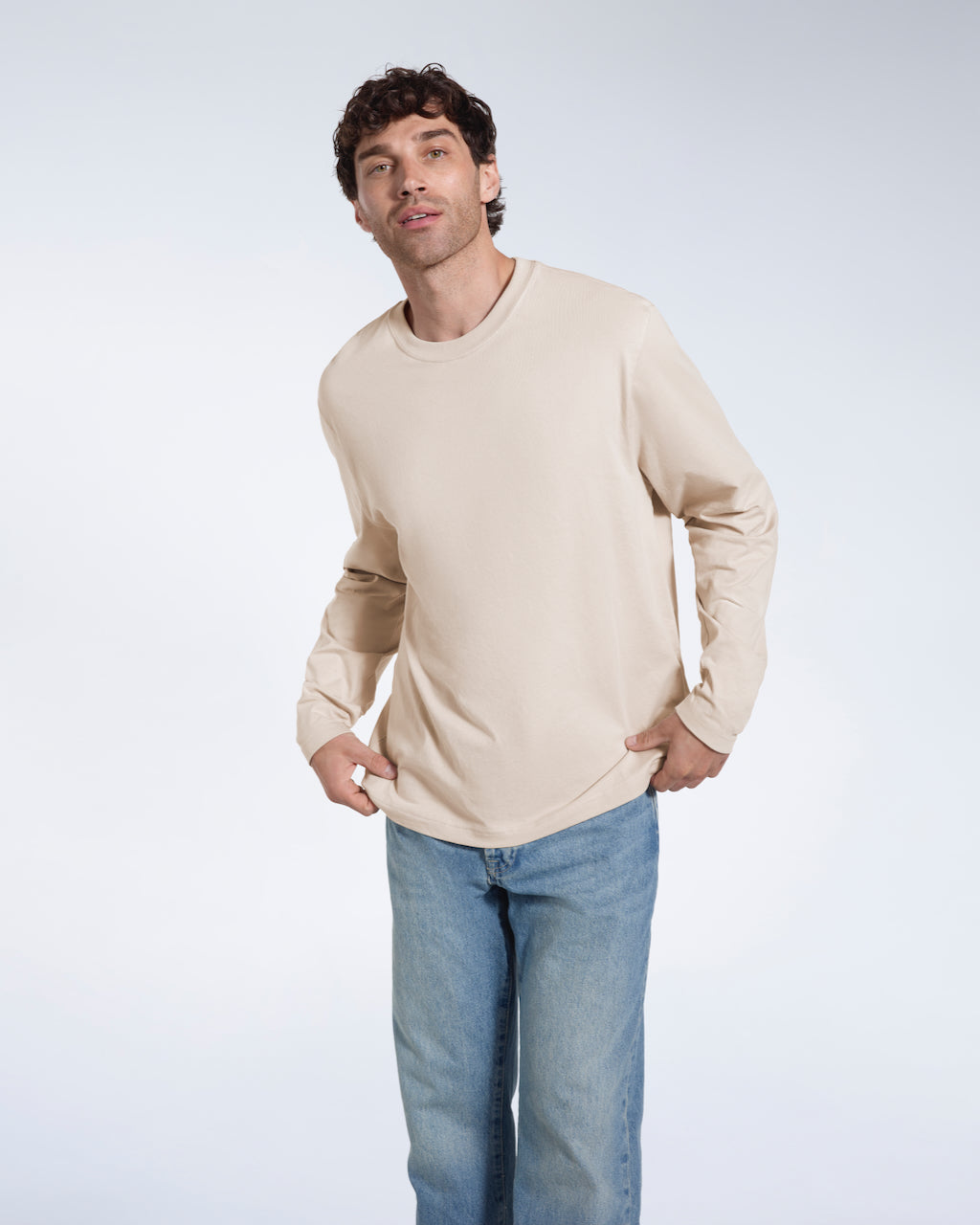 A man looking into the camera, touching the bottom of his plain stone long sleeve organic cotton t shirt.