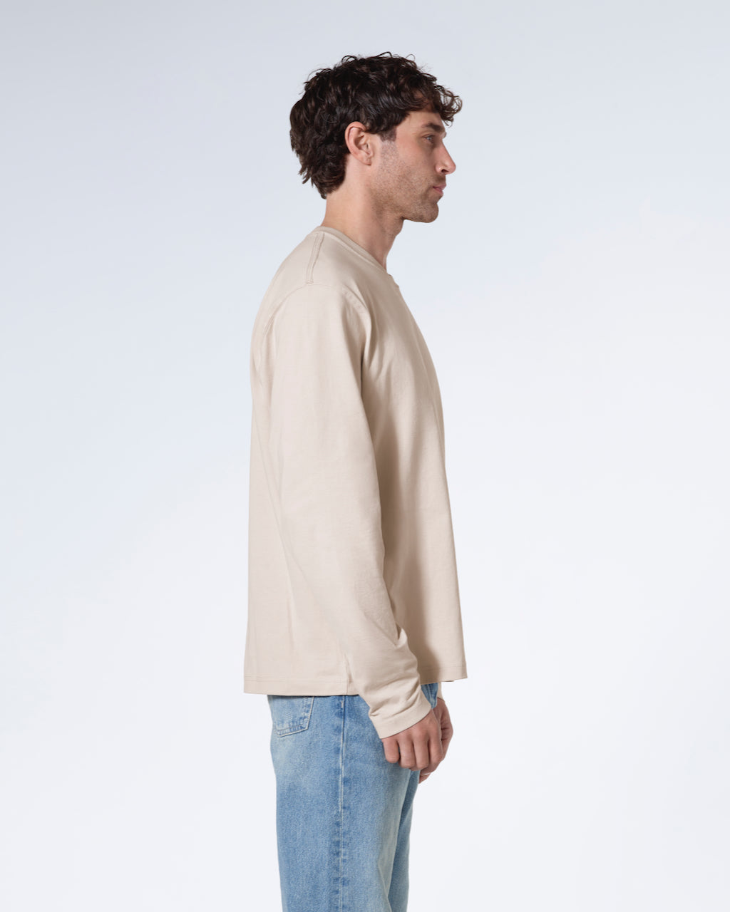 A man facing side on with his arms by his sides, modelling a plain stone long sleeve organic cotton t shirt.