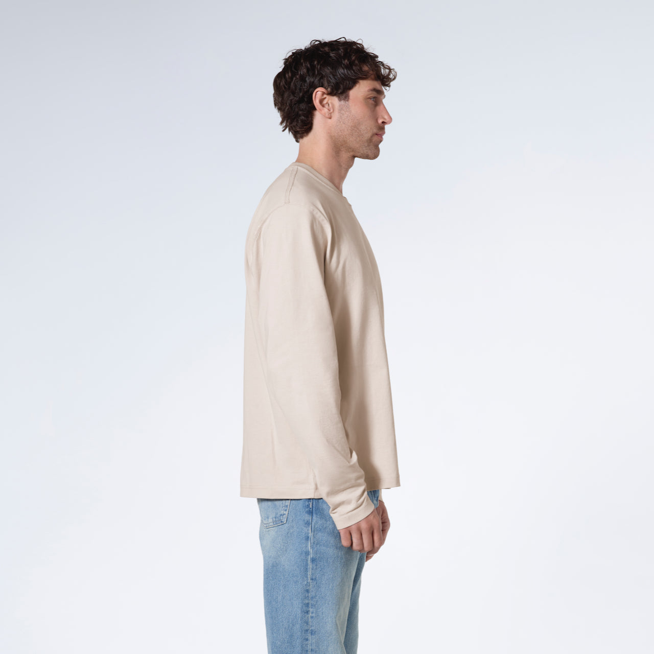 A man facing side on with his arms by his sides, modelling a plain stone long sleeve organic cotton t shirt.