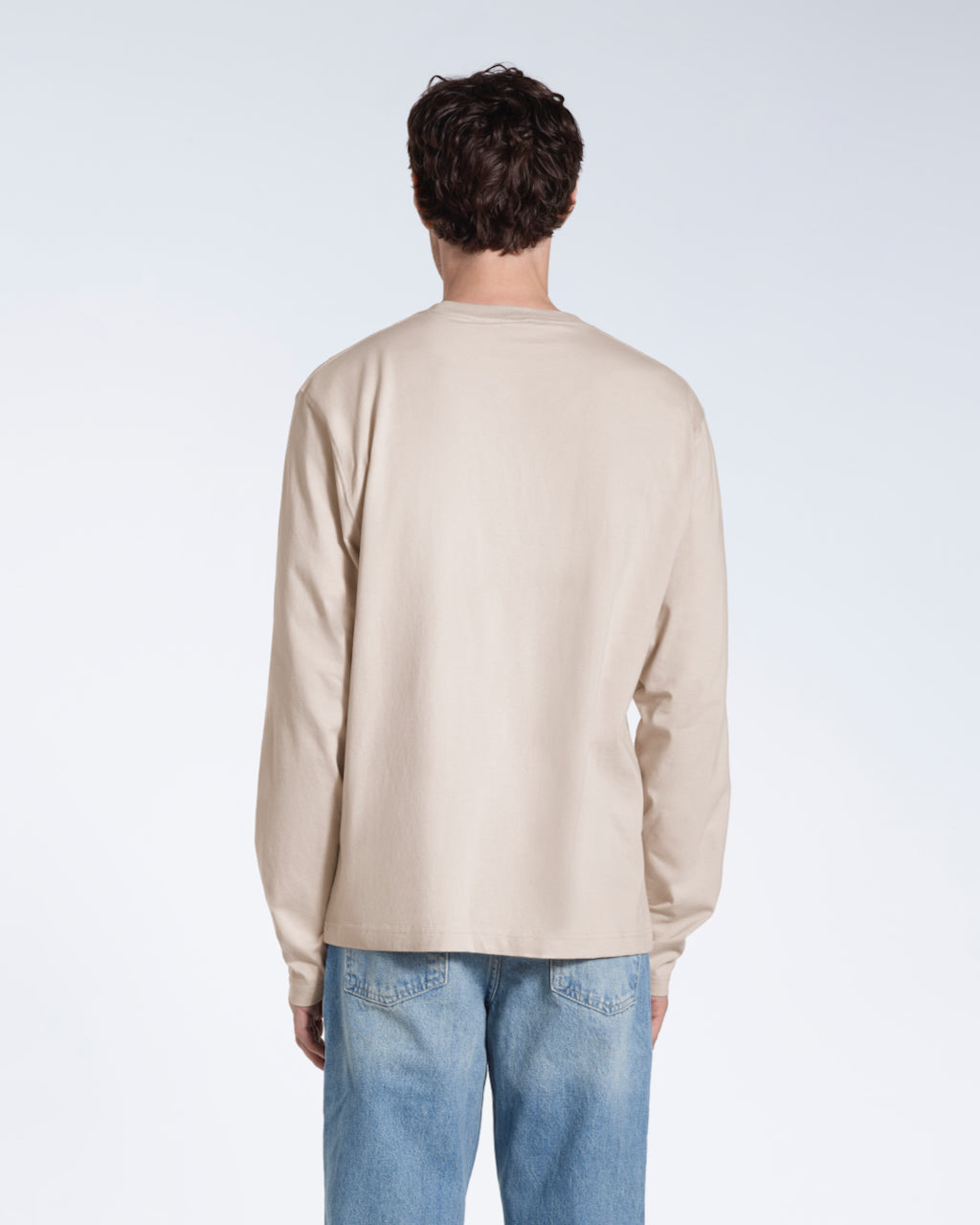 A man facing away from the camera with his arms by his sides, modelling a plain stone long sleeve organic cotton t shirt.