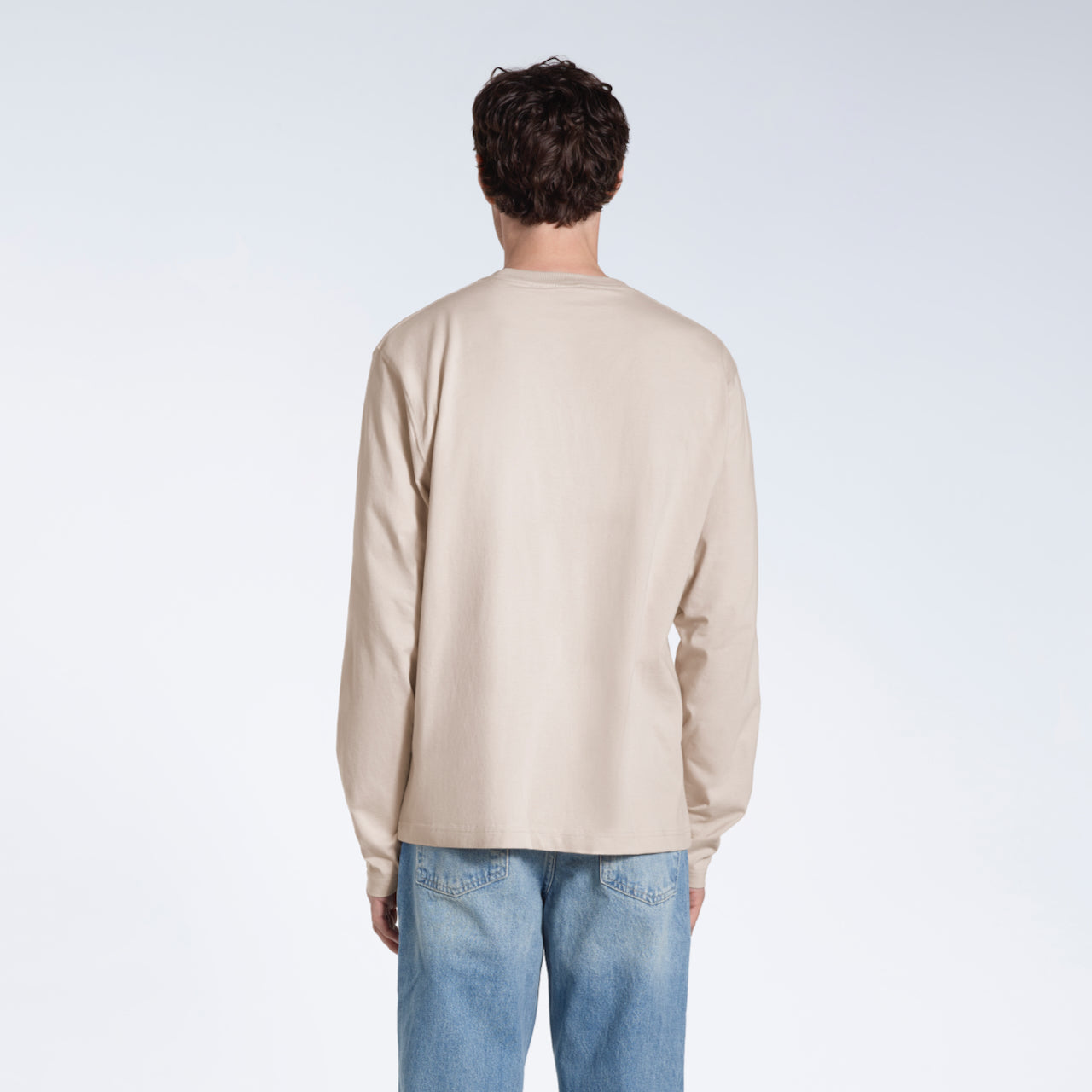 A man facing away from the camera with his arms by his sides, modelling a plain stone long sleeve organic cotton t shirt.