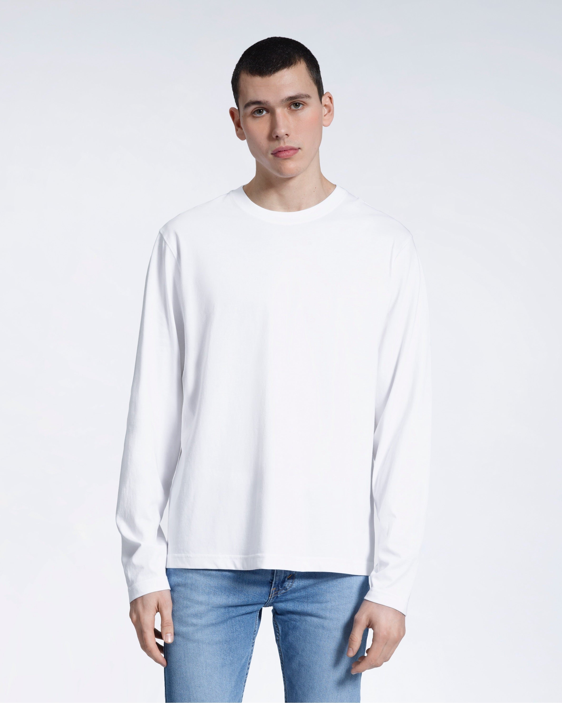 A man standing front on with his arms by his sides, modelling a plain white long sleeve organic cotton t shirt.
