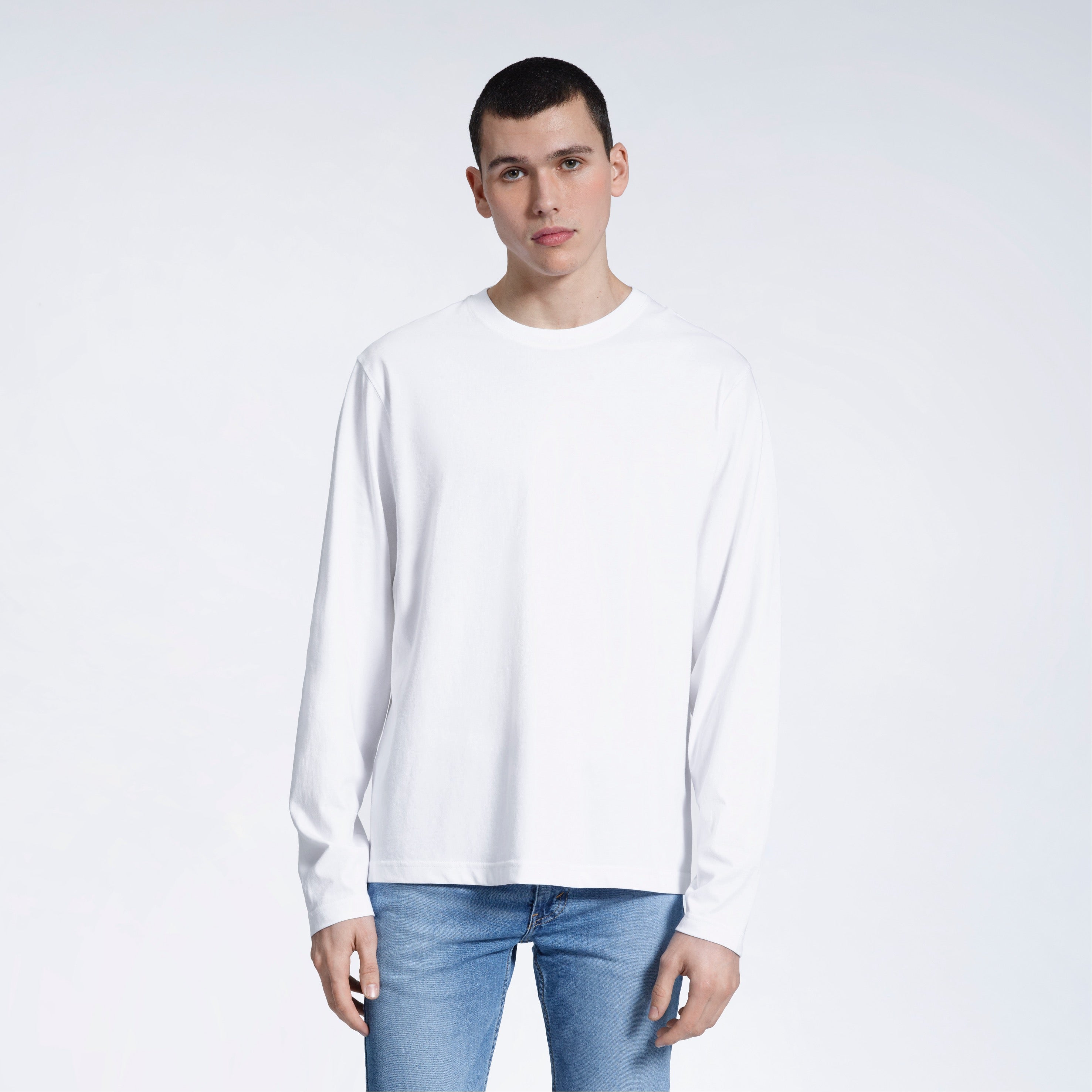 A man standing front on with his arms by his sides, modelling a plain white long sleeve organic cotton t shirt.