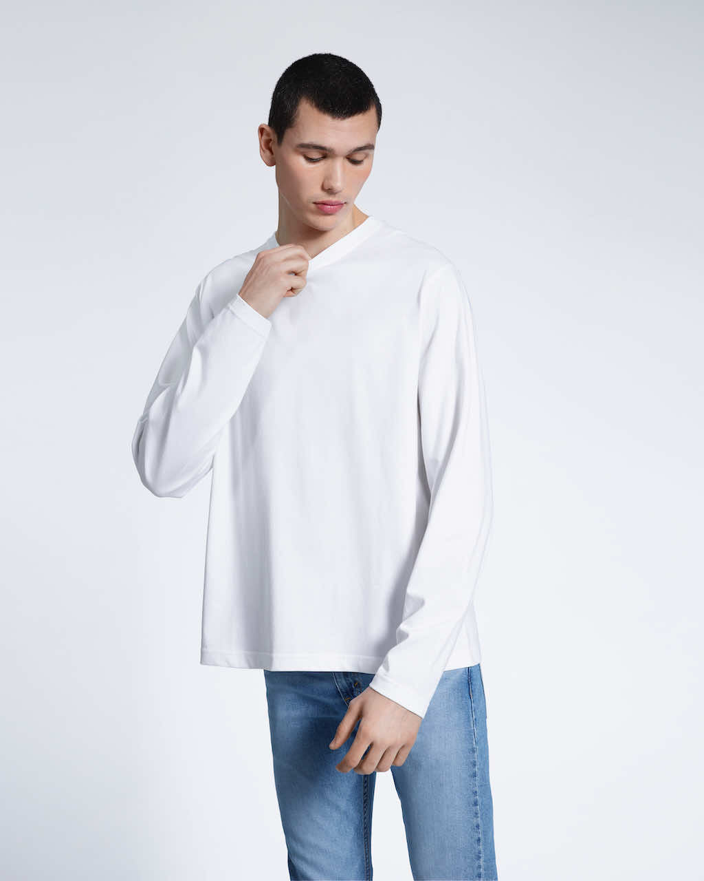 A man looking down touching his collar, modelling a plain white long sleeve organic cotton t shirt.