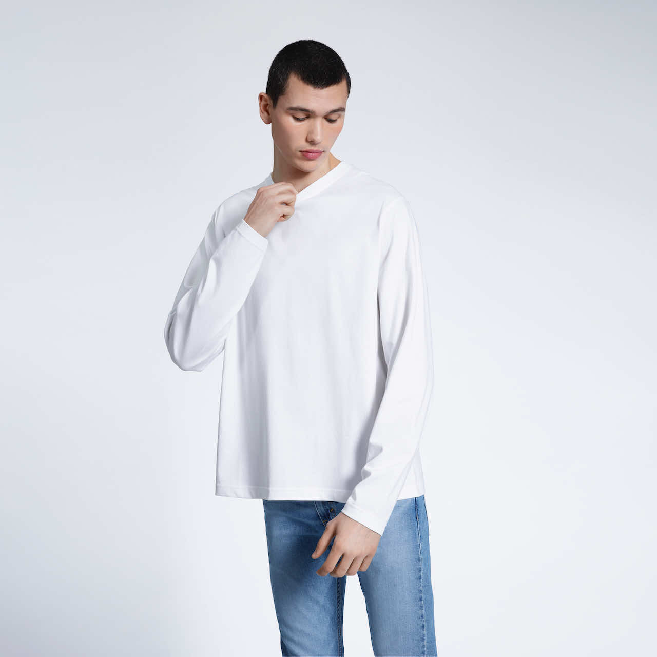 A man looking down touching his collar, modelling a plain white long sleeve organic cotton t shirt.