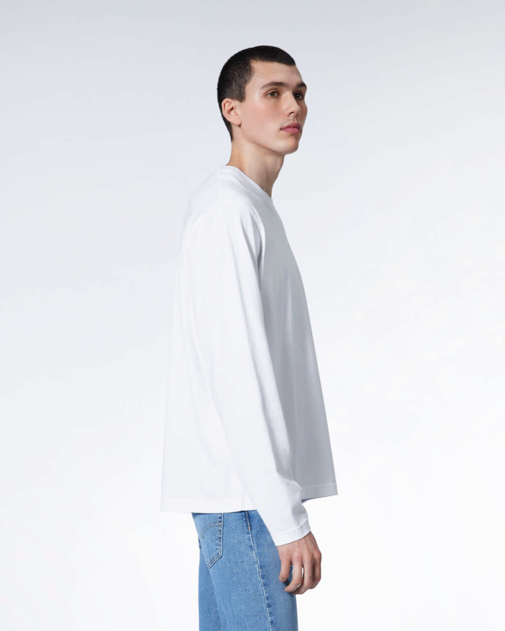 A man facing side on with his arms by his sides, modelling a plain white long sleeve organic cotton t shirt.