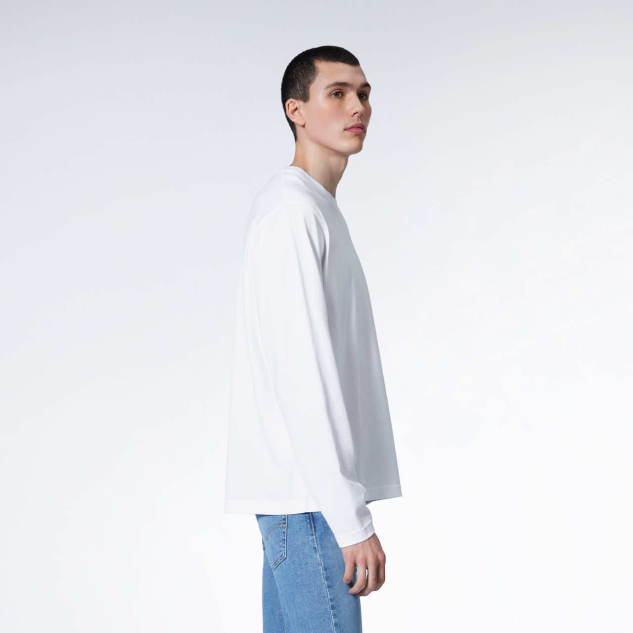 A man facing side on with his arms by his sides, modelling a plain white long sleeve organic cotton t shirt.