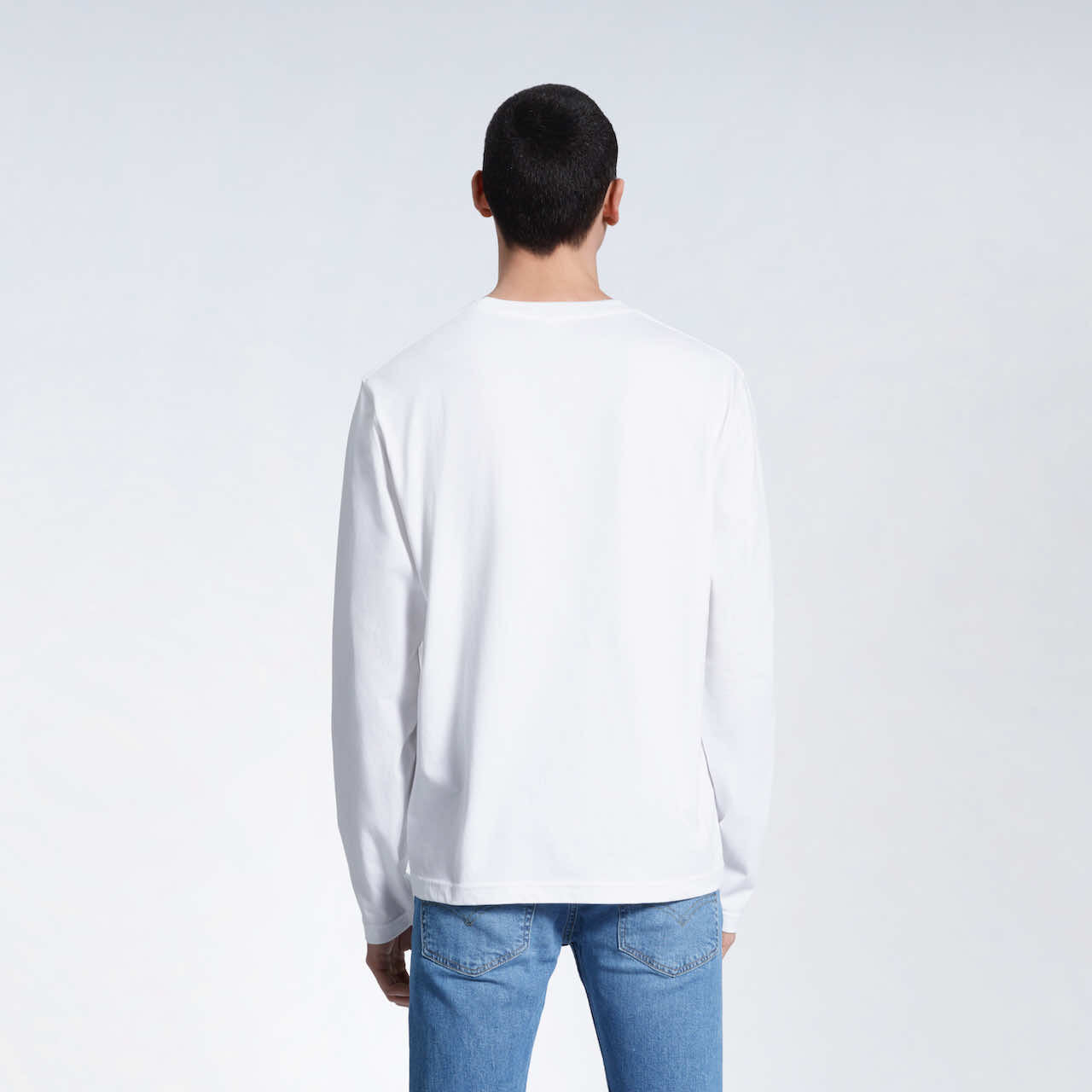 A man standing front on with his arms by his sides, modelling a plain white long sleeve organic cotton t shirt.