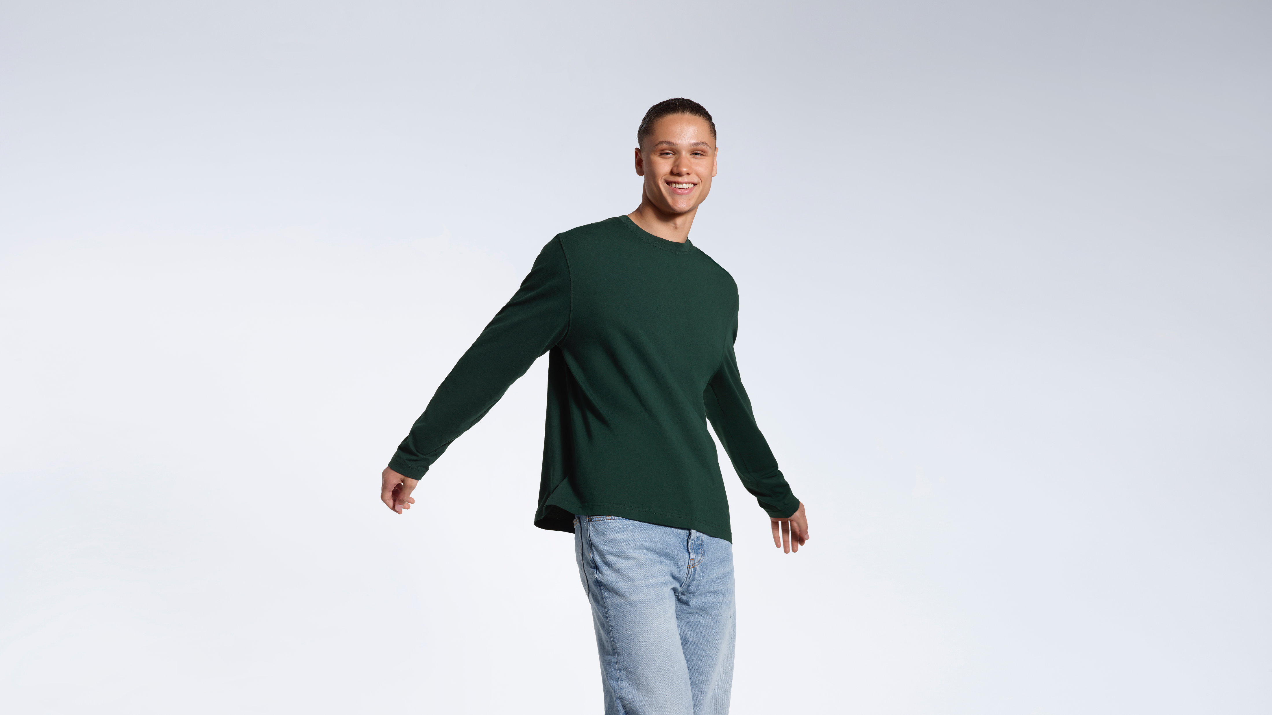 A man smiing into the camera, modelling a plain green, organic cotton, long sleeve t shirt.