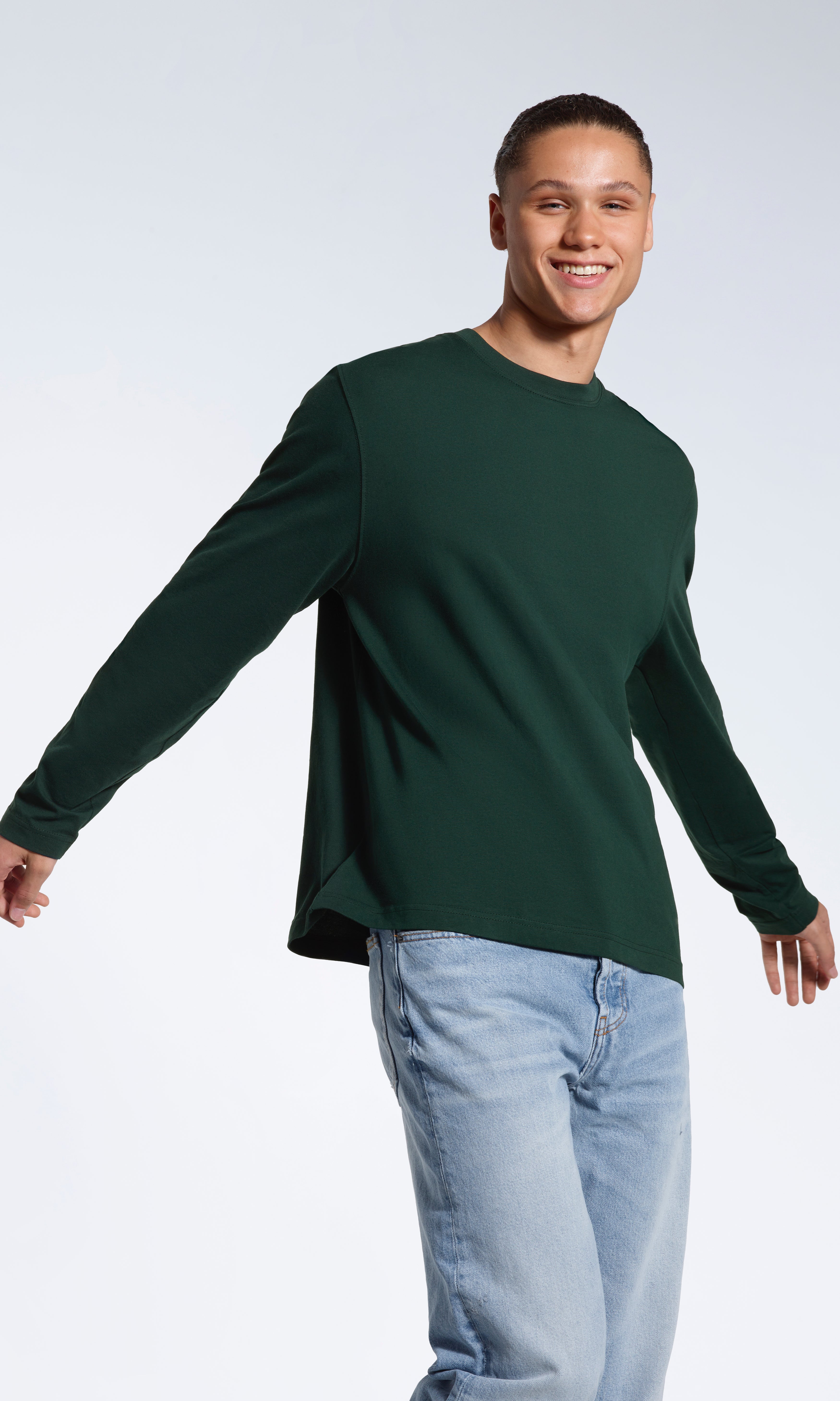 A man smiing into the camera, modelling a plain green, organic cotton, long sleeve t shirt.