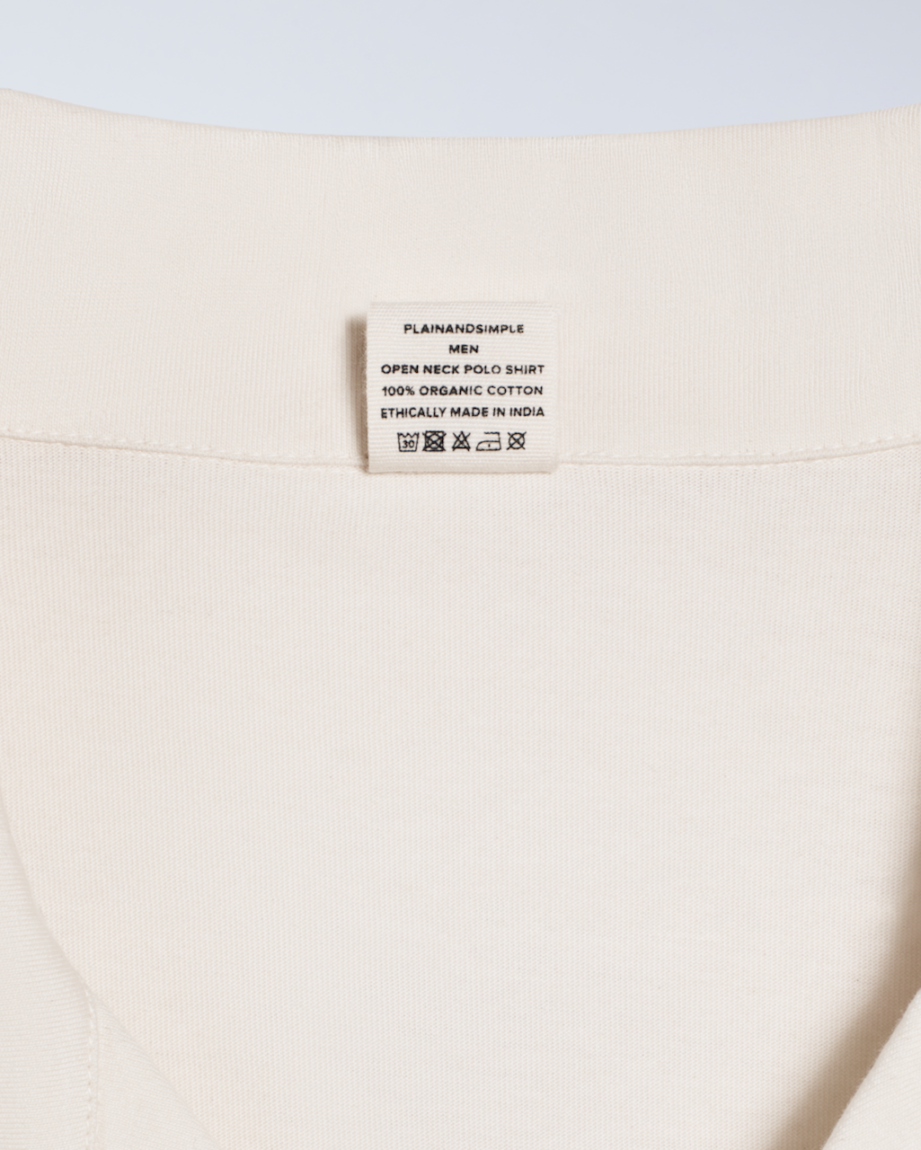A close up of the neck label in a natural coloured, open neck organic cotton polo shirt.