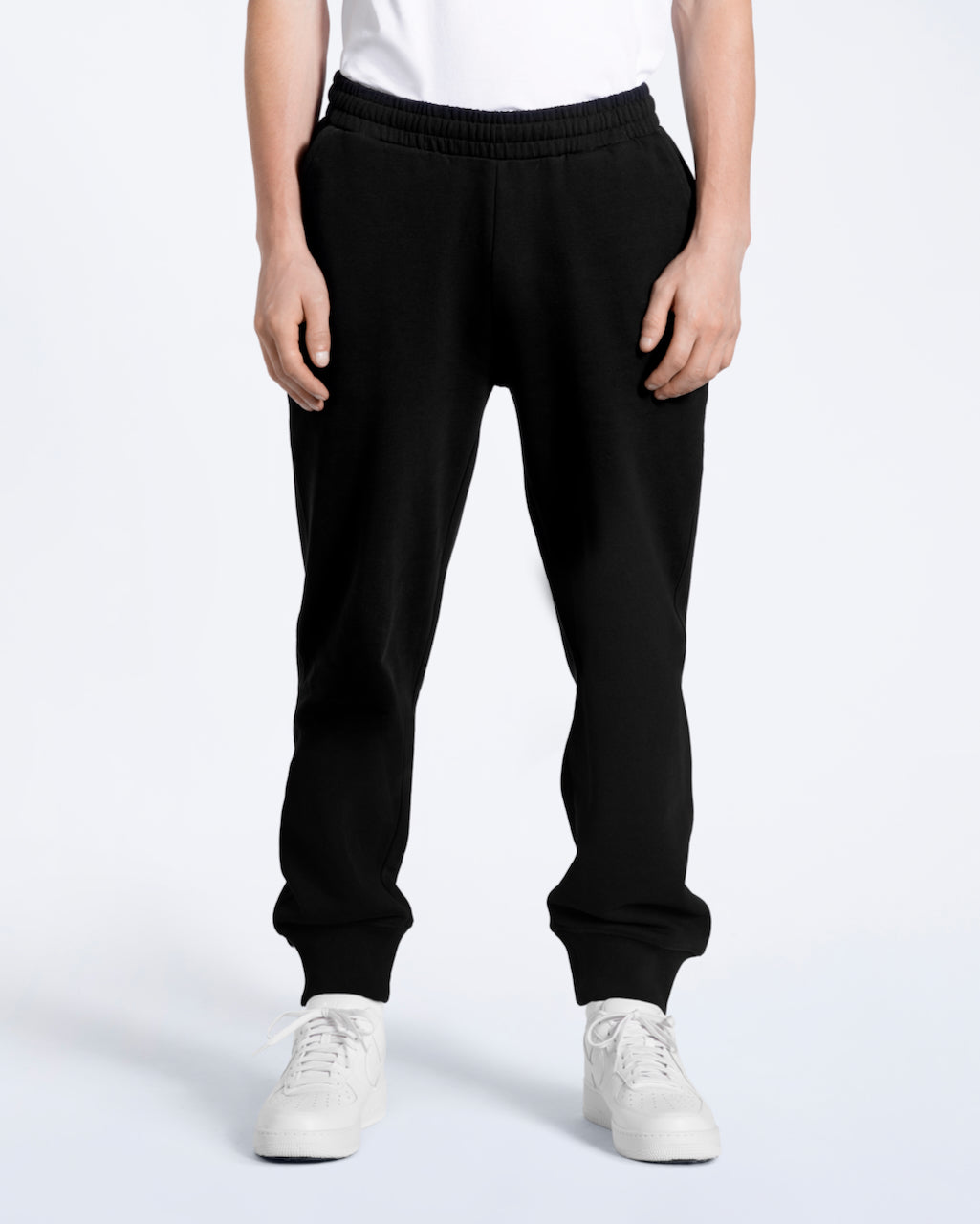 A person with their arms by their sides, modelling a pair of men's black organic cotton joggers.