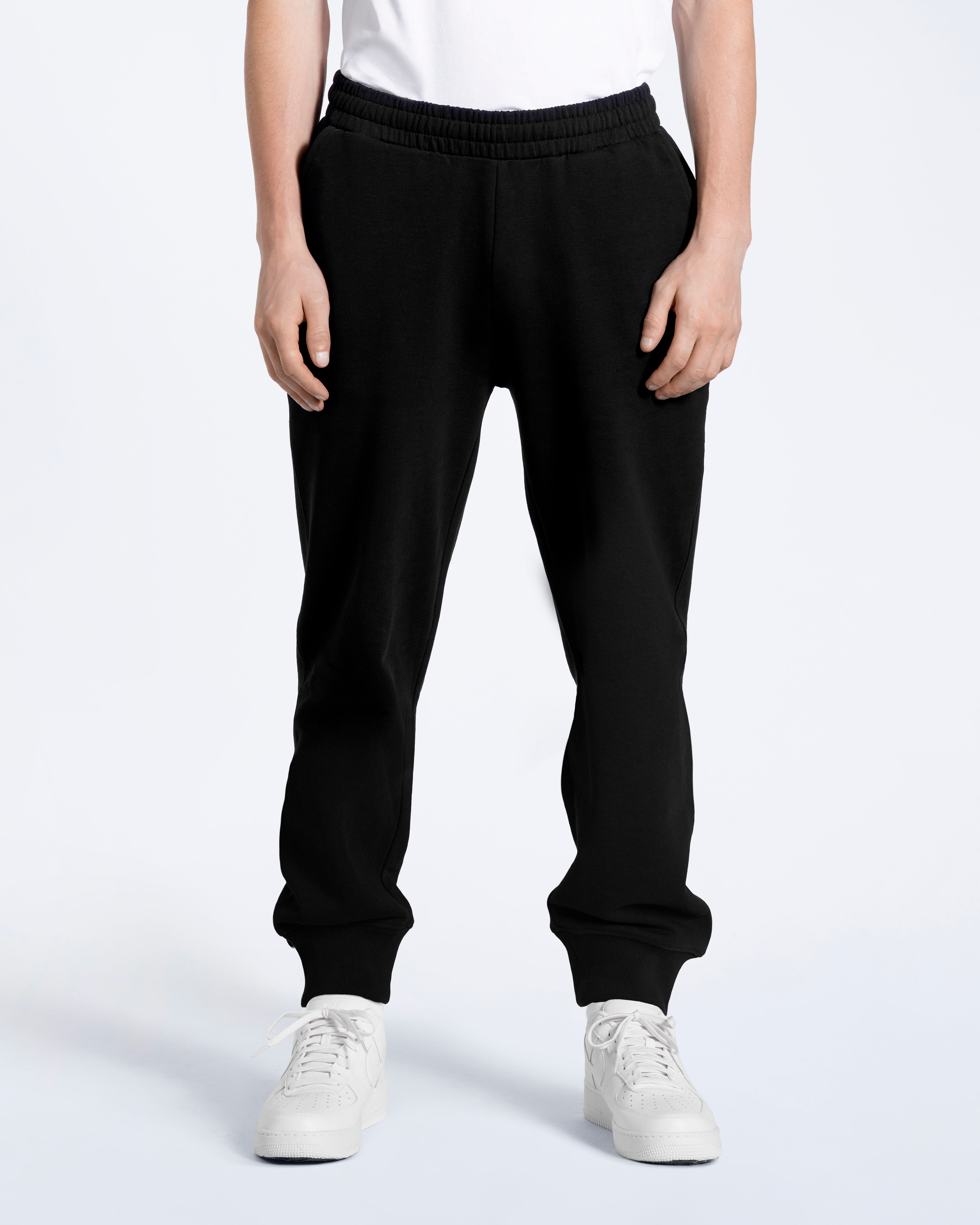 A person with their arms by their sides, modelling a pair of men's black organic cotton joggers.