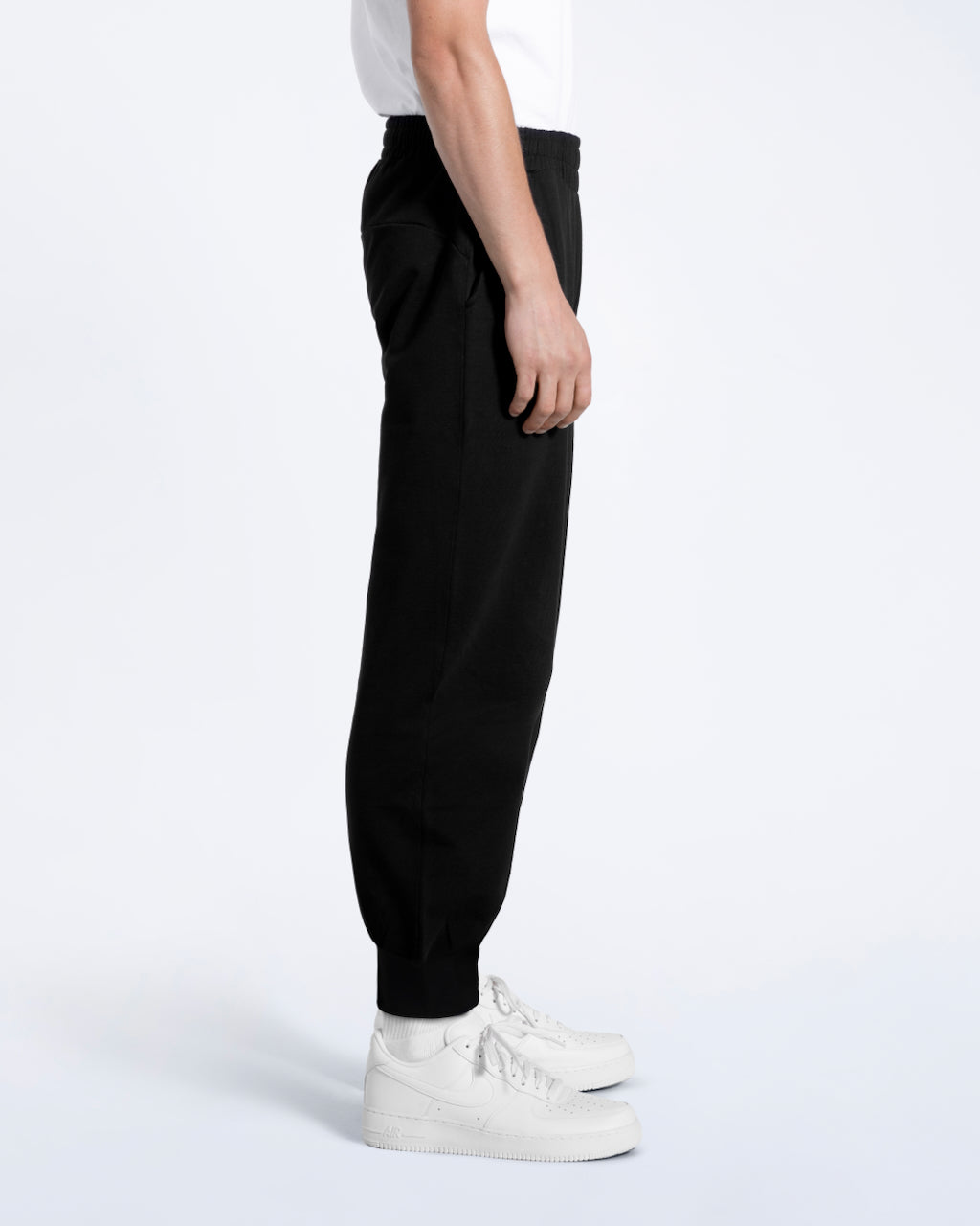 A man facing side on with his arms by his sides, modelling a pair of black organic cotton joggers.