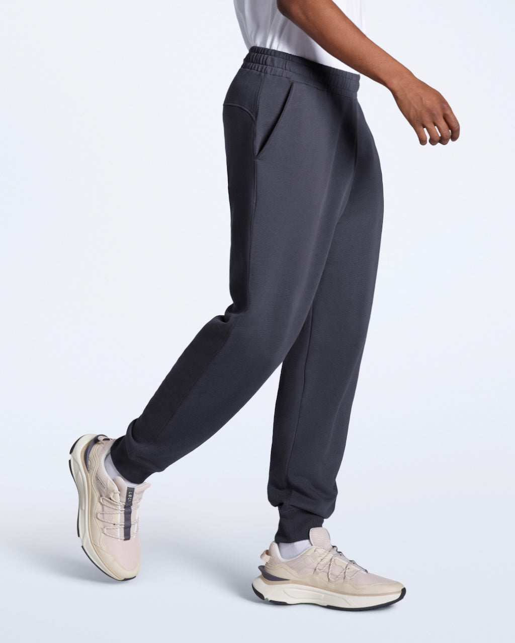 A man mid walk, modelling a pair of dark grey organic cotton joggers.