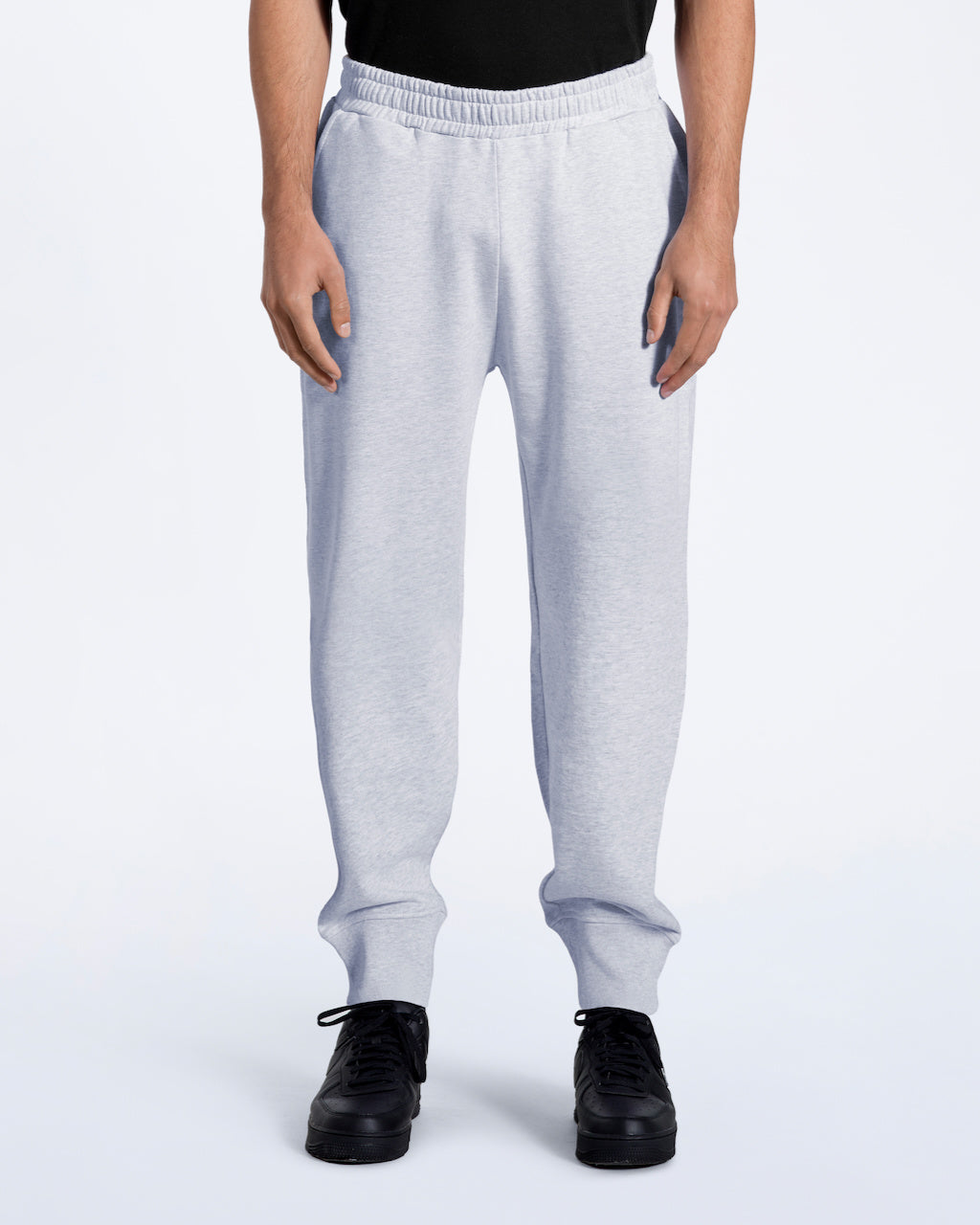 A man facing front on with his arms by his sides, modelling a pair of plain grey, organic cotton joggers.