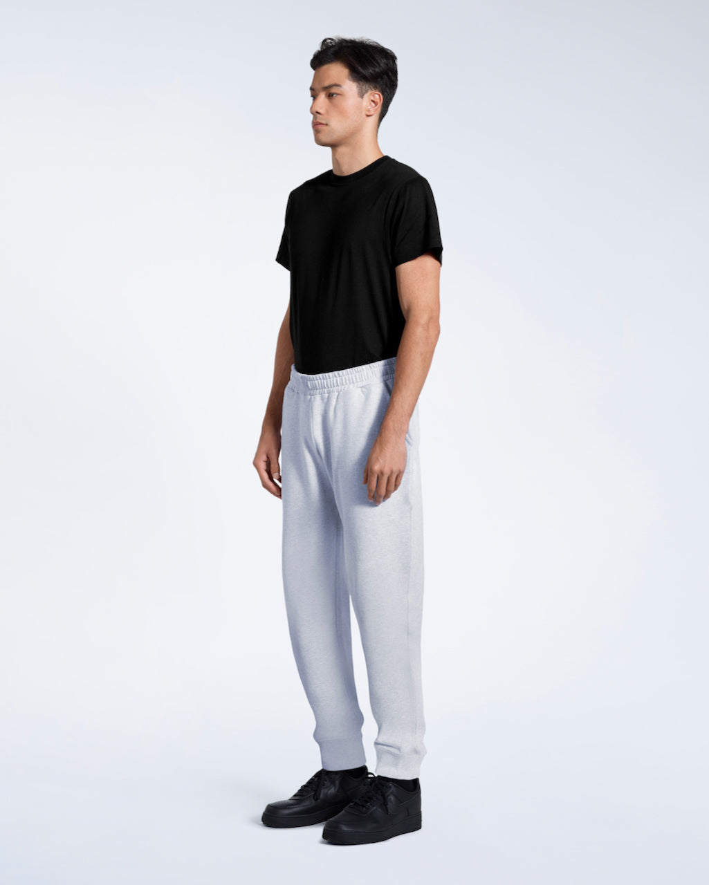 A man at an angle with his arms by his sides, modelling a pair of plain grey, organic cotton joggers with a black t shirt.