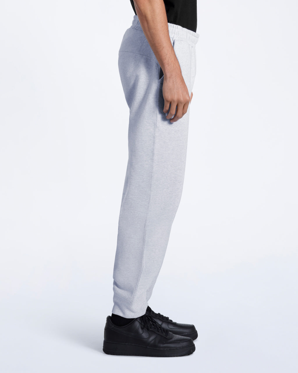 A man facing side on with his arms by his sides, modelling a pair of plain grey, organic cotton joggers.