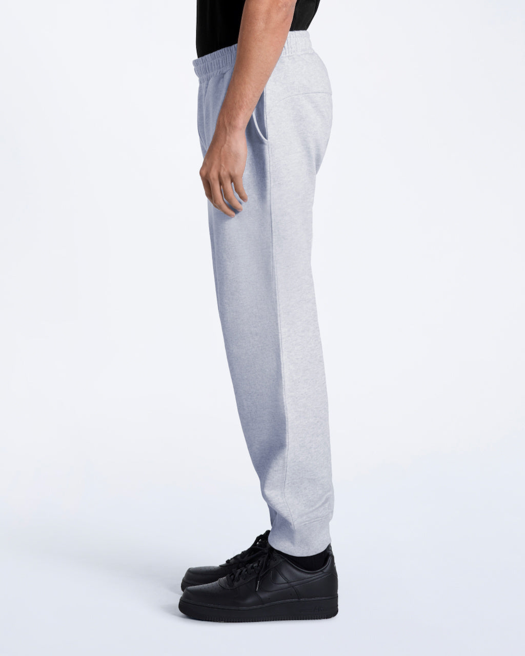 A man facing side on with his arms by his sides, modelling a pair of plain grey, organic cotton joggers.
