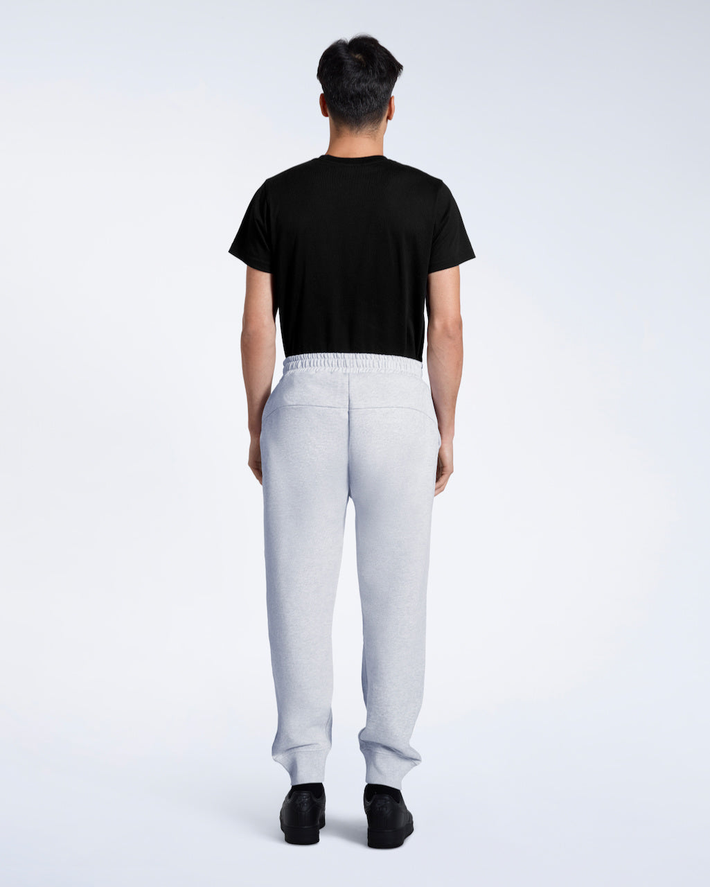 A man facing away from the camera with his arms by his sides, modelling a pair of plain grey, organic cotton joggers with a black t shirt.