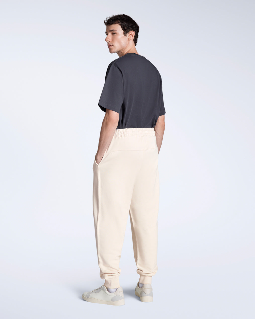 A man with his back to the camera looking over his shoulder with his hands in his pockets, modelling a pair of natural organic cotton joggers.