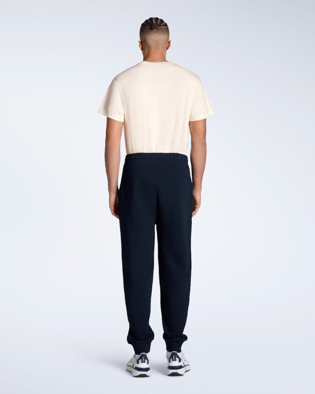 A man with his back to the camera with his arms by his sides, modelling a pair of navy organic cotton joggers.