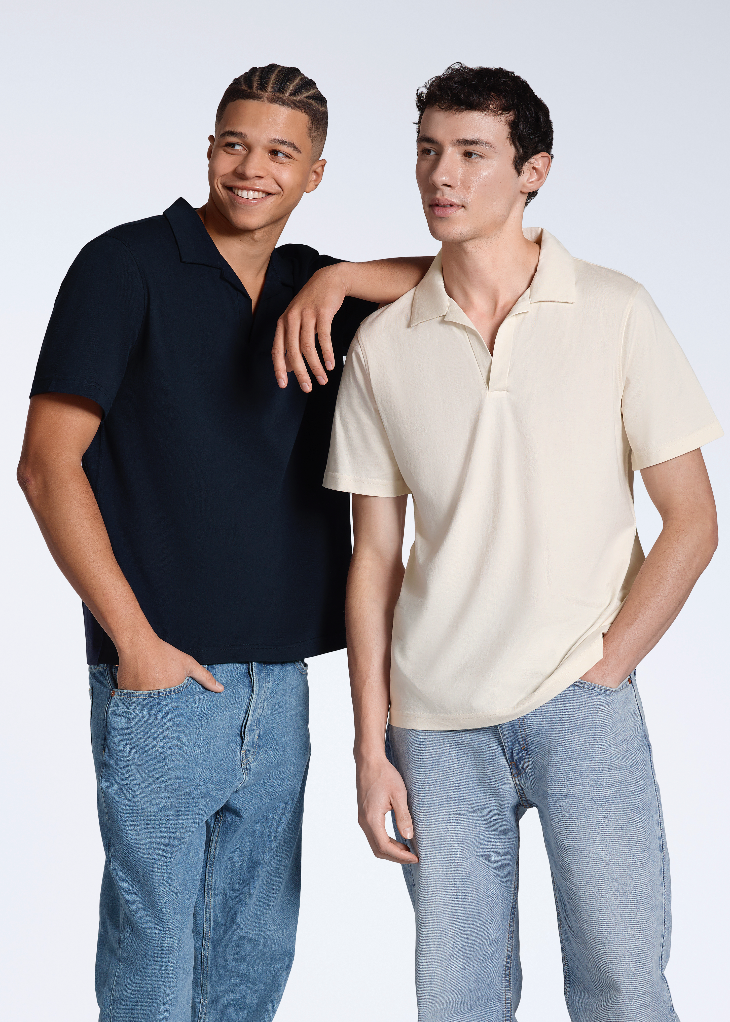 Two men looking away from the camera, modelling plain navy and natural, organic cotton polo shirts.