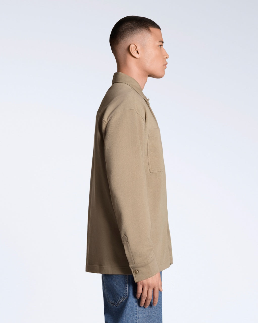 A man facing side on, modelling a plain beige, organic cotton overshirt.