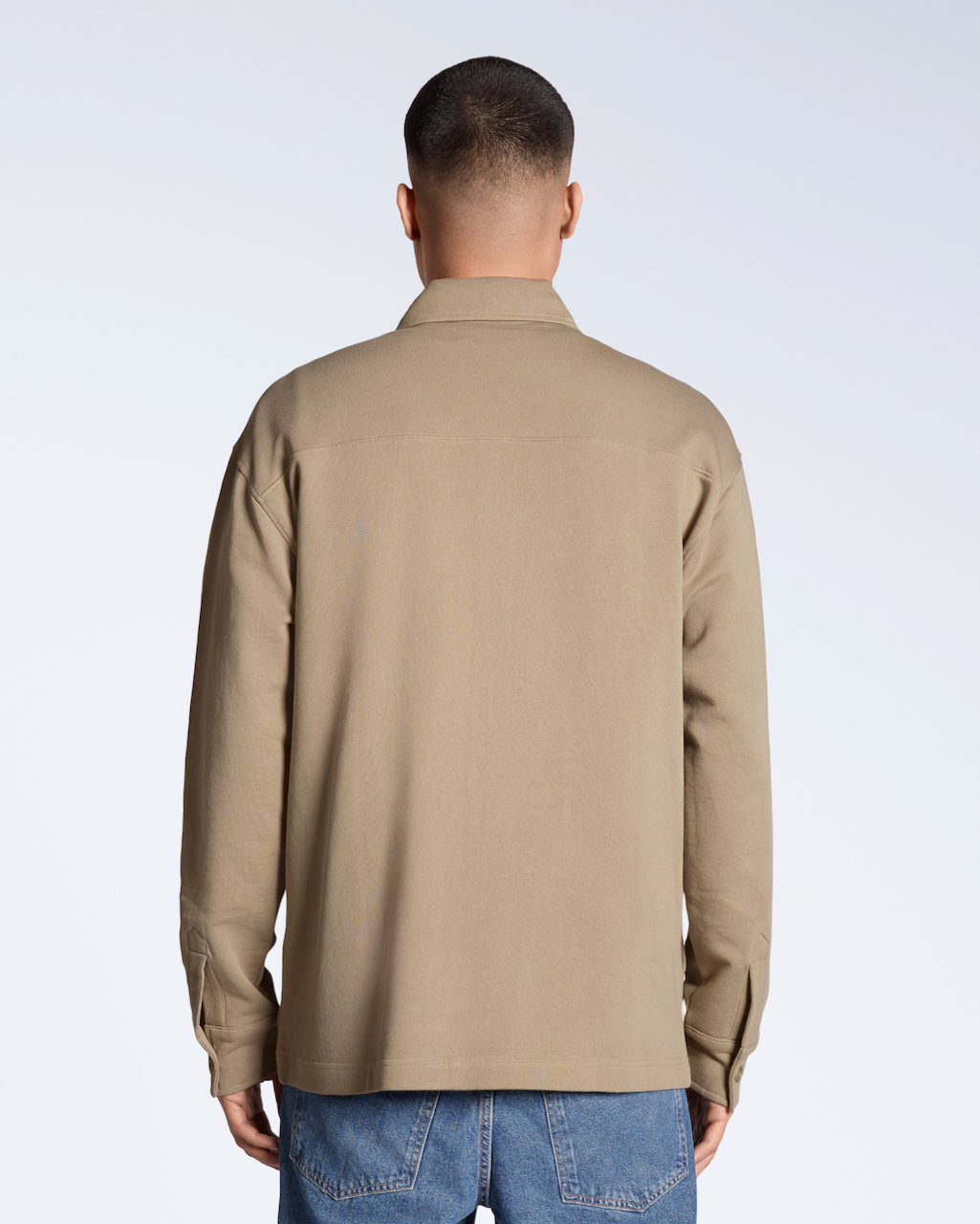A man facing away from the camera, modelling a plain beige, organic cotton overshirt.