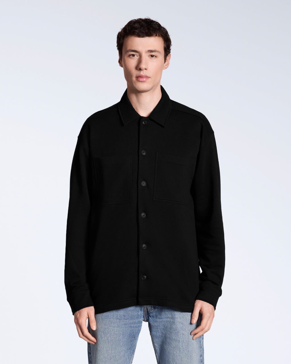 A man facing front on looking into the camera, modelling a plain black organic cotton overshirt.