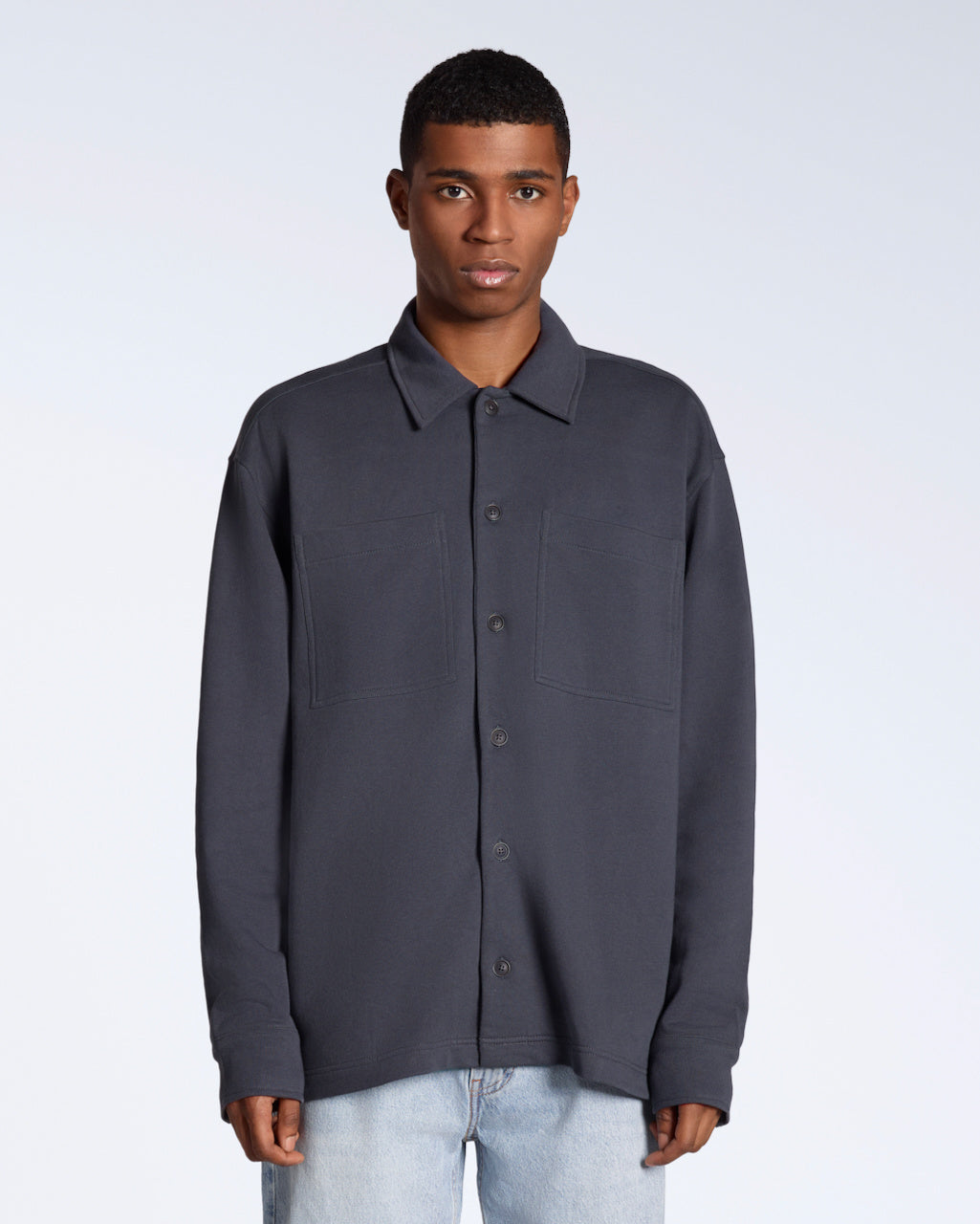 A man facing front on looking into the camera, modelling a plain dark grey organic cotton overshirt.
