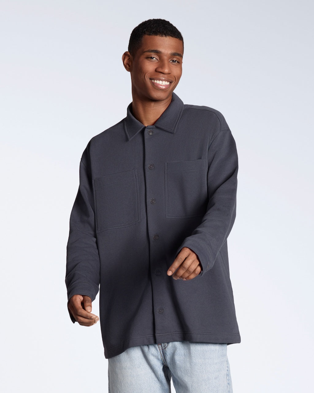 A man smiling into the camera, modelling a plain dark grey, organic cotton overshirt.