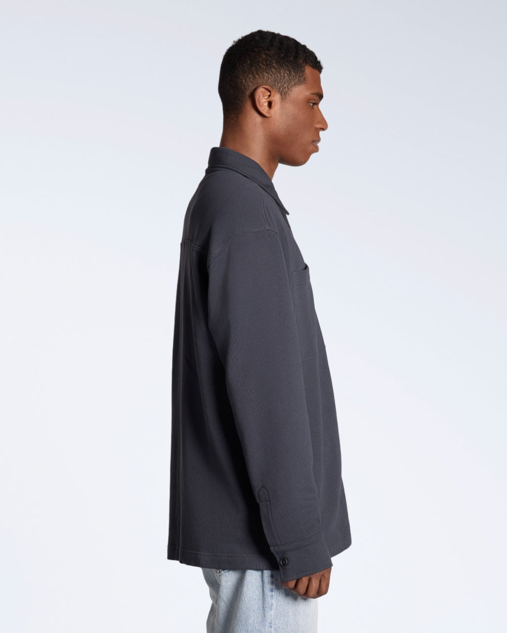 A man facing side on, modelling a plain dark grey, organic cotton overshirt.