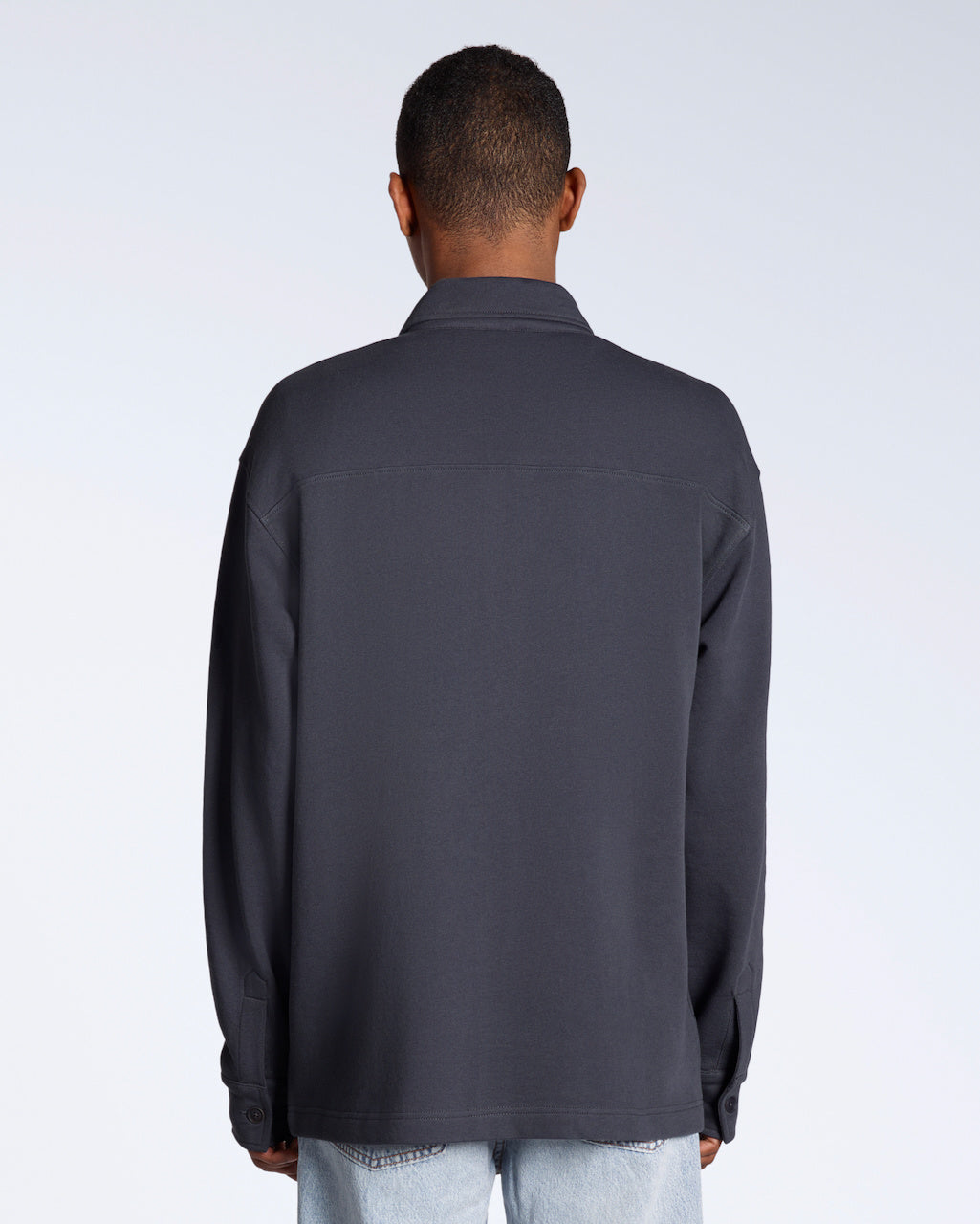 A man facing away from the camera, modelling a plain dark grey, organic cotton overshirt.