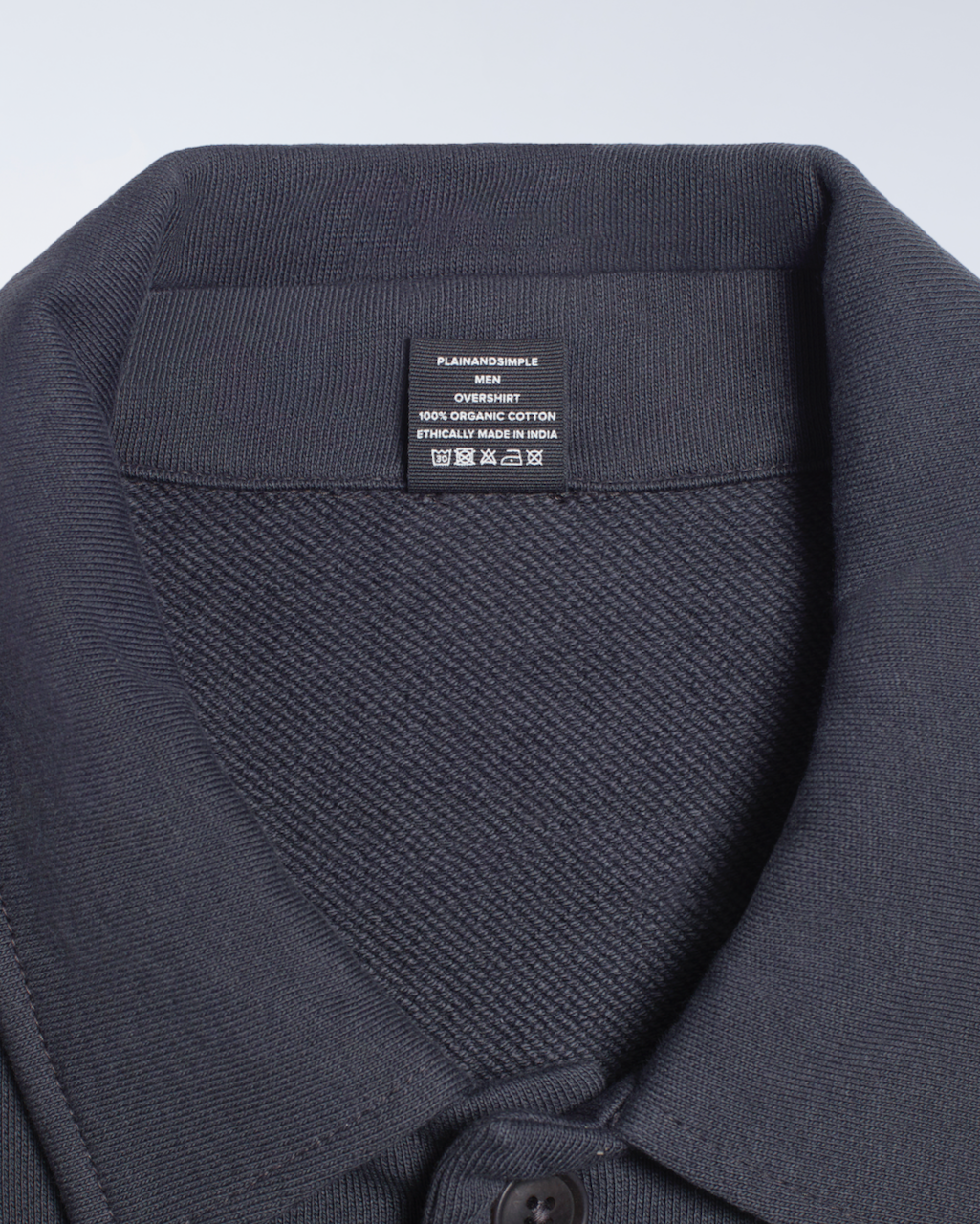 A close up of the neck label in a dark grey, organic cotton overshirt.