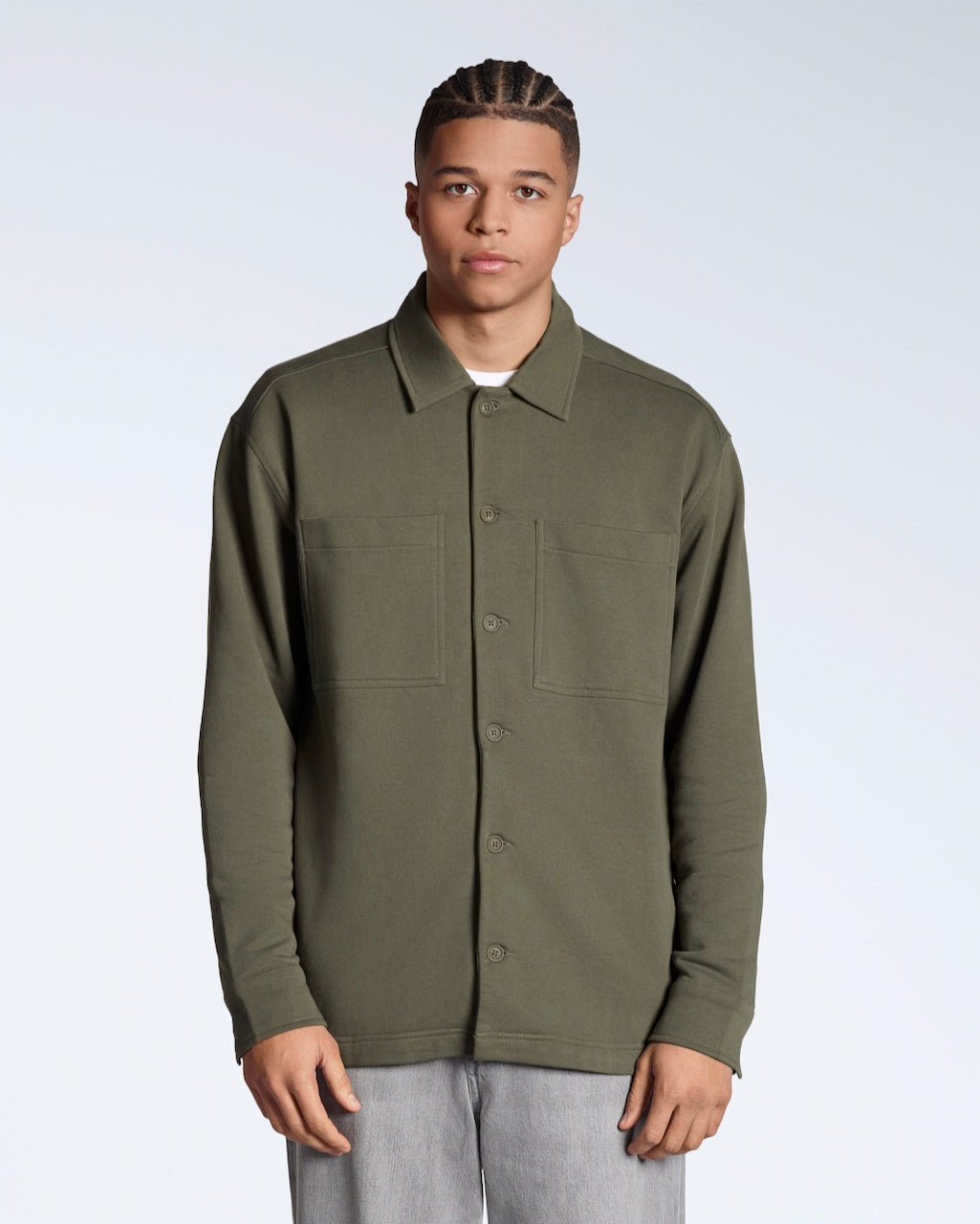 A man facing front on looking into the camera, modelling a plain olive coloured, organic cotton overshirt.
