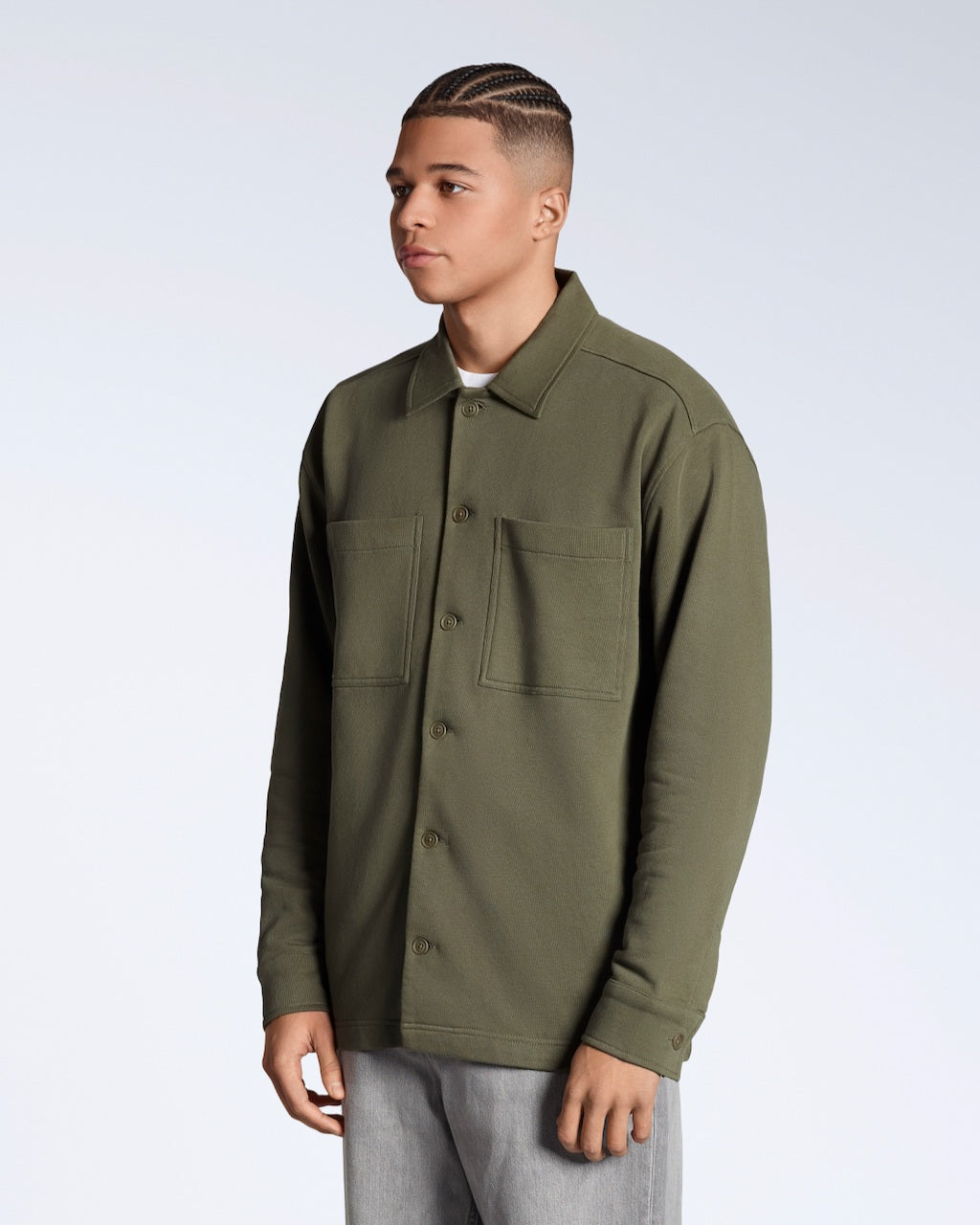 A man at an angle with his arms by his sides, modelling a plain olive coloured, organic cotton overshirt.