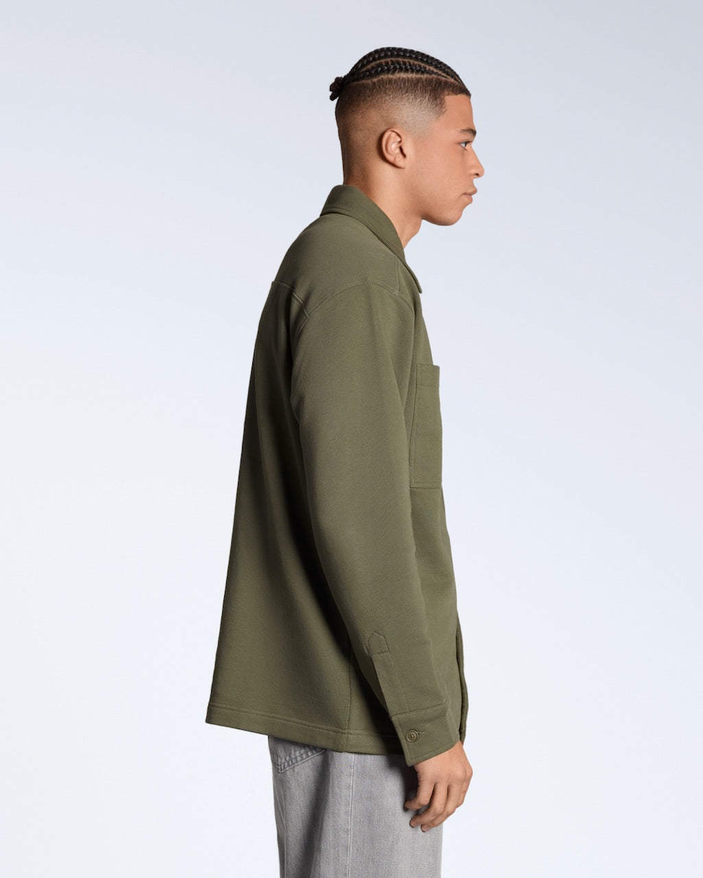 A man facing side on, modelling a plain olive coloured, organic cotton overshirt.