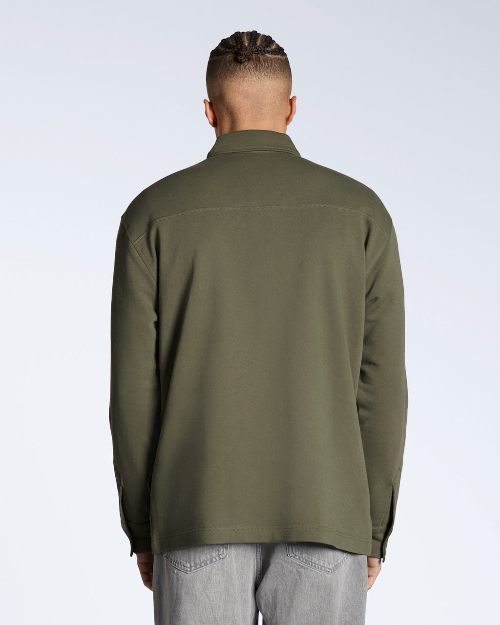 A man facing away from the camera, modelling a plain olive coloured, organic cotton overshirt.