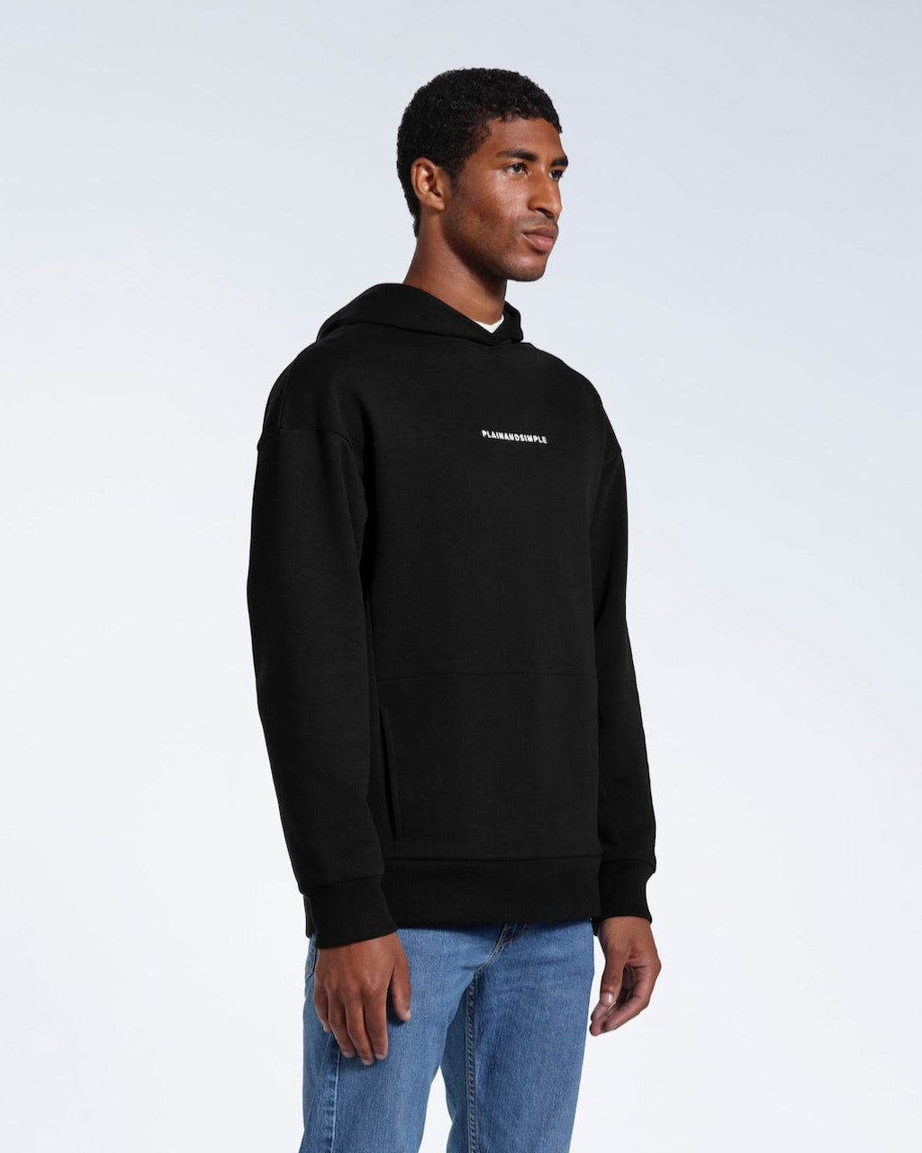 A man at an angle looking away from the camera, modelling a branded black oversized heavyweight organic cotton hoodie.