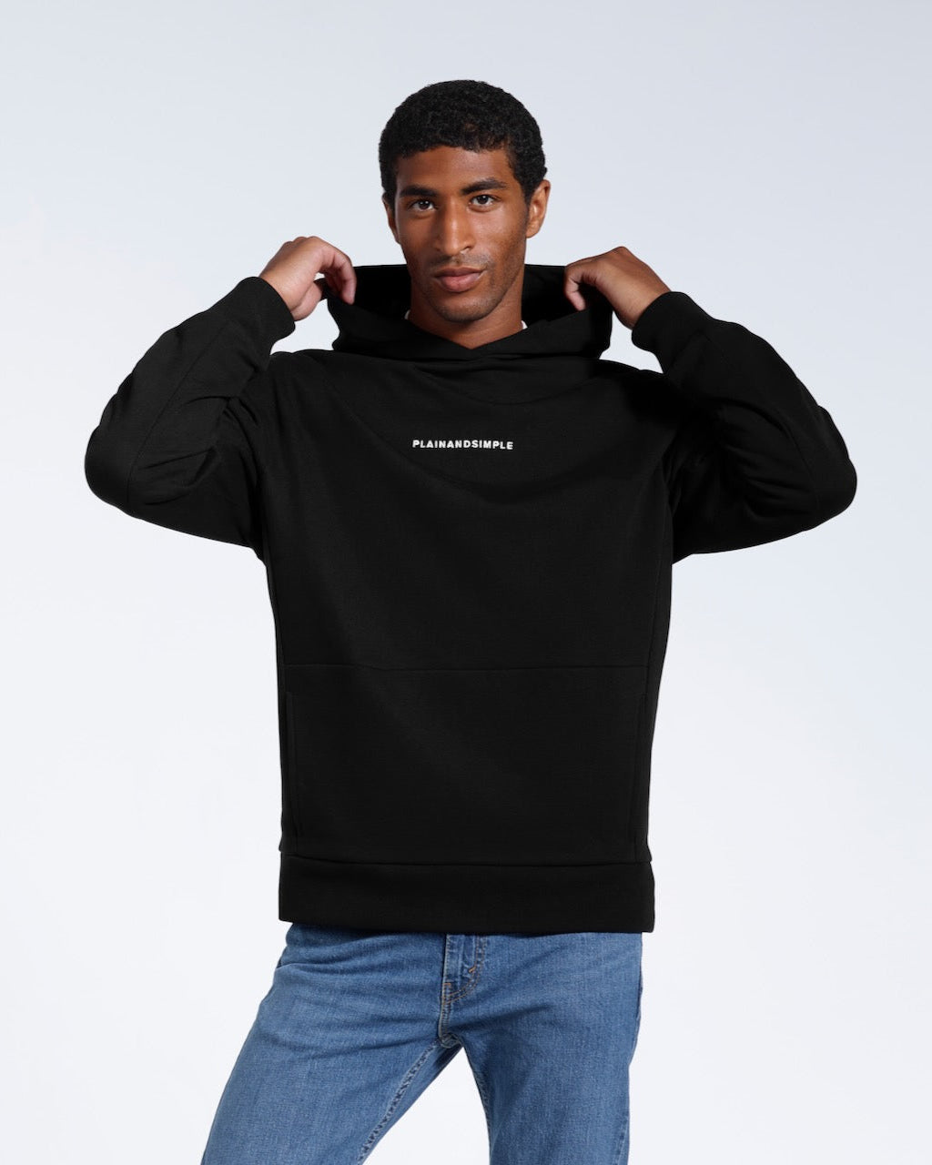 A man touching his hood and looking into the camera, modelling a branded black oversized heavyweight organic cotton hoodie.
