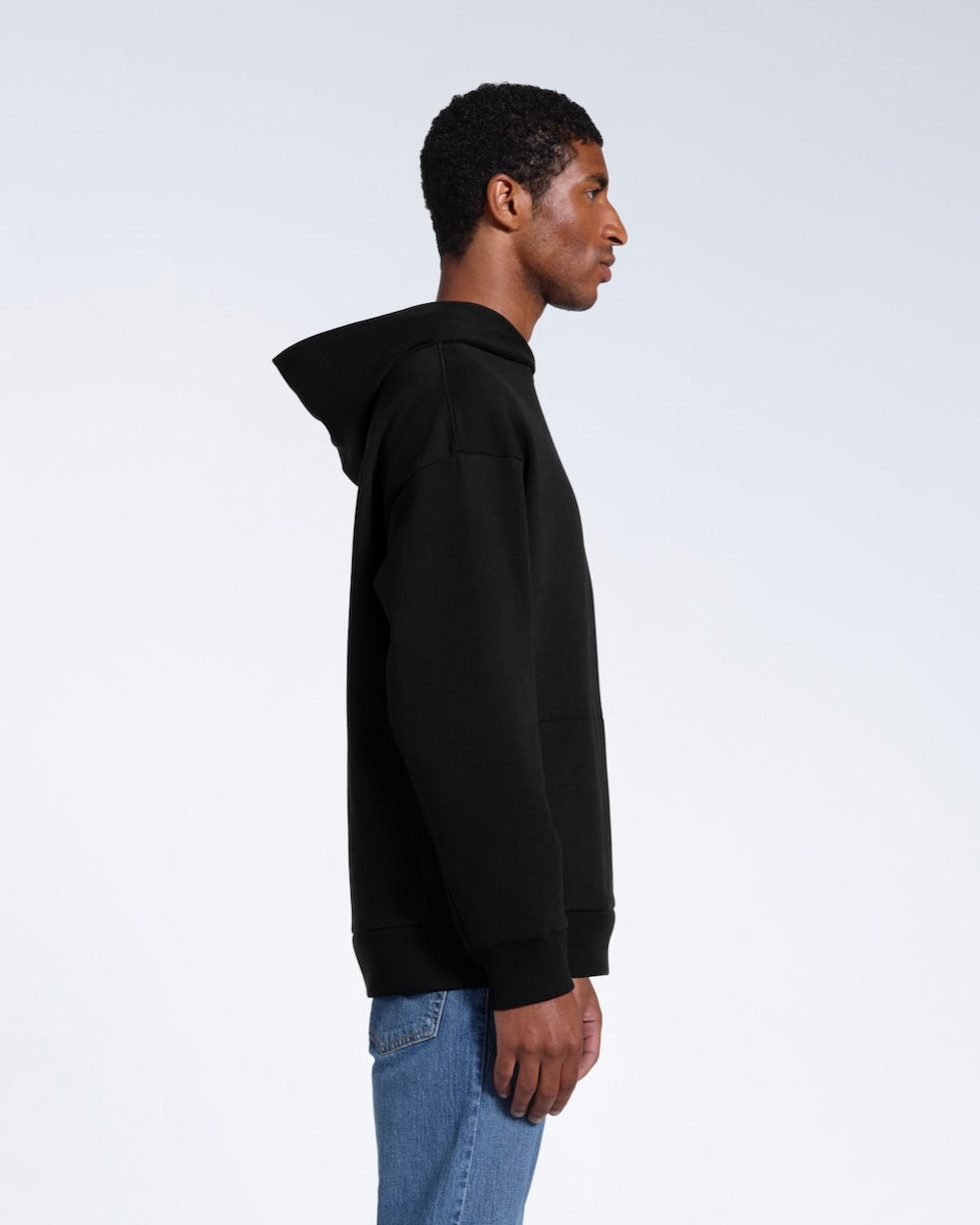 A man facing side on, modelling a black oversized heavyweight organic cotton hoodie.