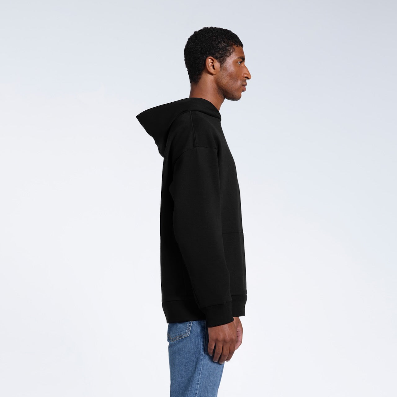 A man facing side on, modelling a black oversized heavyweight organic cotton hoodie.