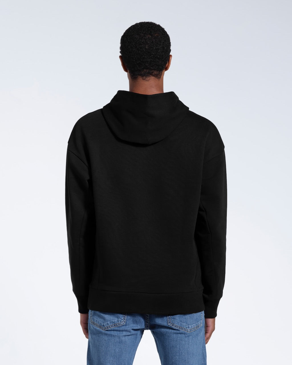 A man facing away from the camera with his arms by his sides, modelling a black oversized heavyweight organic cotton hoodie.